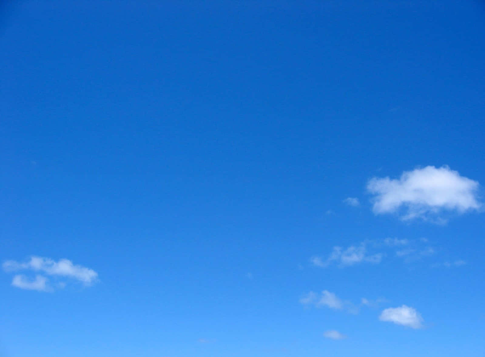 Blue Skies 桌布 壁紙 — 廣闊清澈的藍天，點綴著散落的蓬鬆白雲，懶洋洋地飄過。