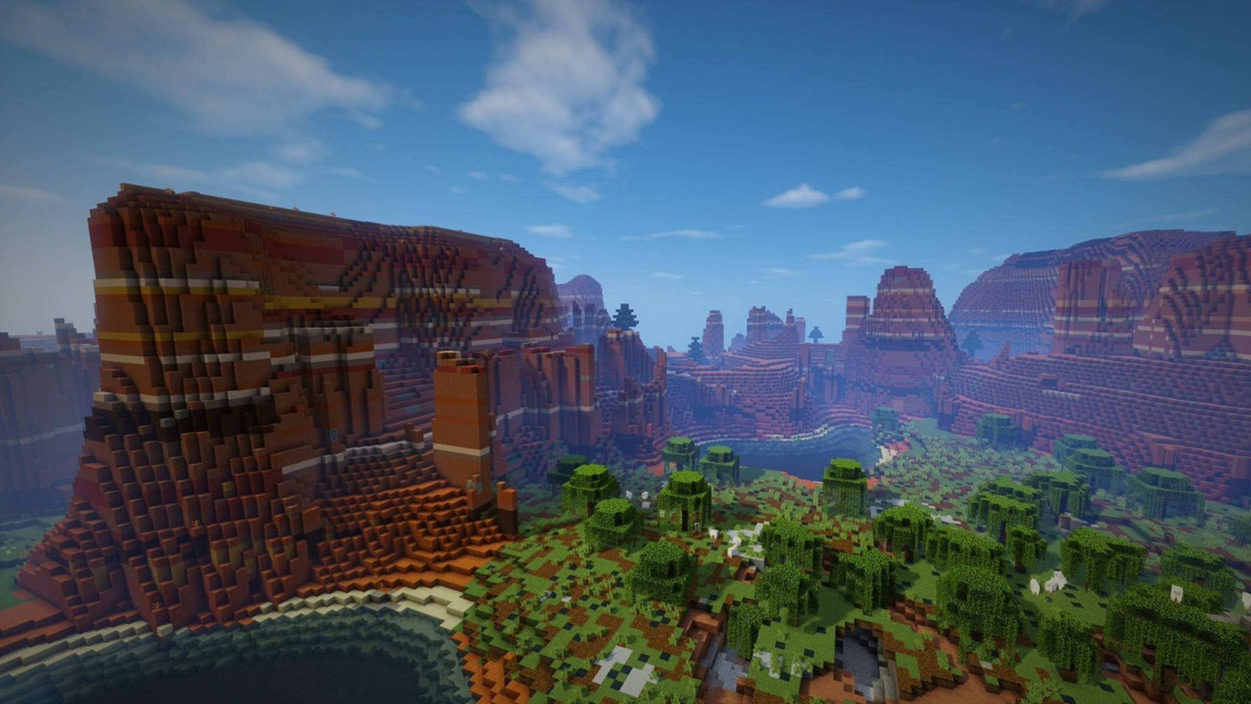 Minecraft Shaders 桌布 壁紙 — 廣闊的像素化峽谷景觀，分層的紅色岩層和茂密的綠樹，在明亮的藍天下。
