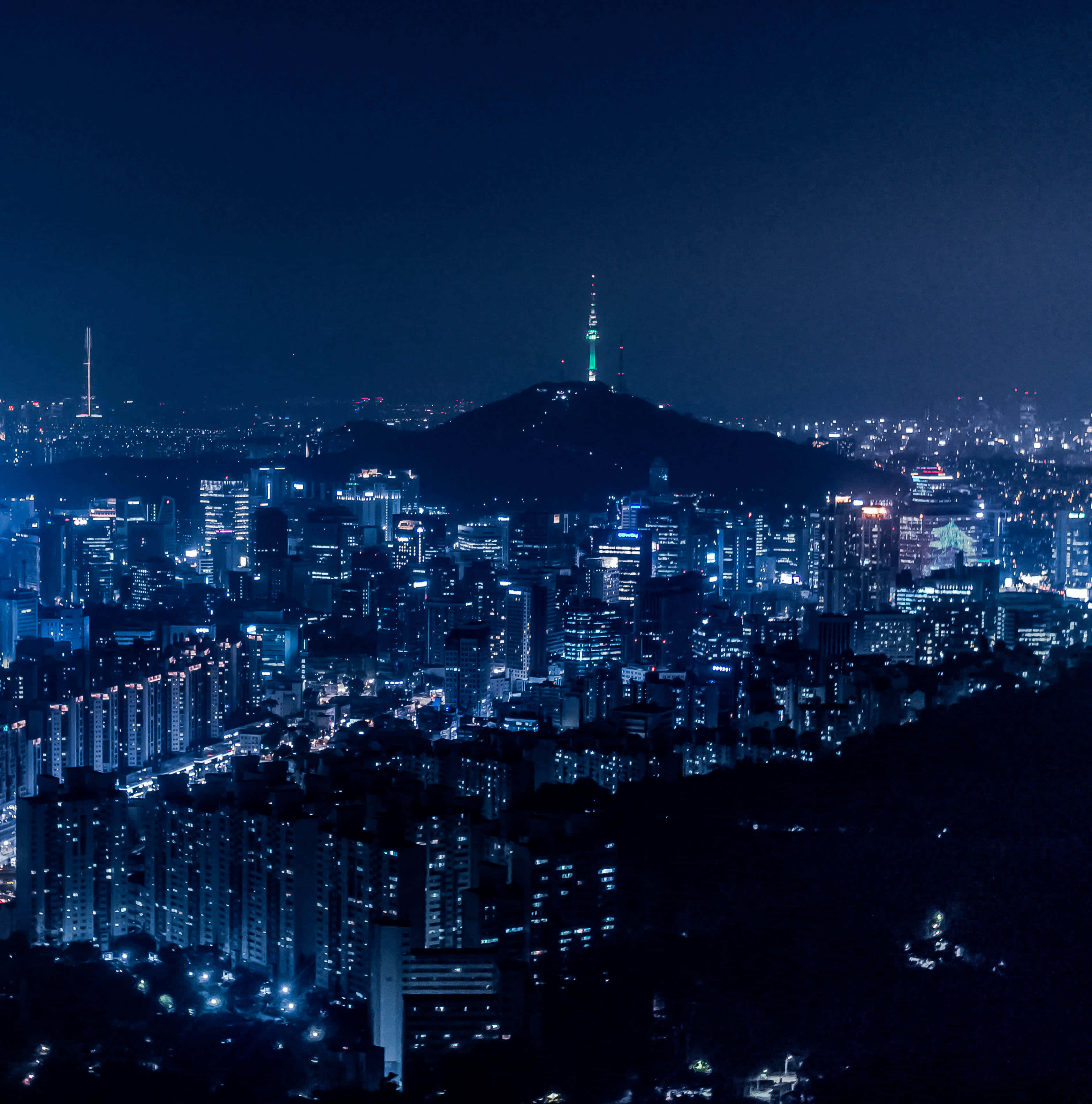 South Korea 桌布 壁紙 — 廣闊的夜景城市景觀，閃爍的摩天大樓和一座山頂上點亮的塔樓，在黑暗的天空下。