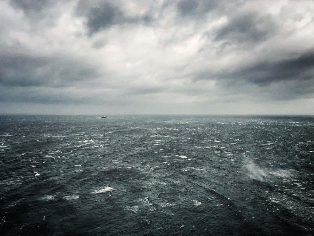 Horizon 桌布 壁紙 — 廣闊的暴風雨海洋，天空佈滿沉重的灰色雲層，遠方一艘船隻在地平線上幾乎看不見。