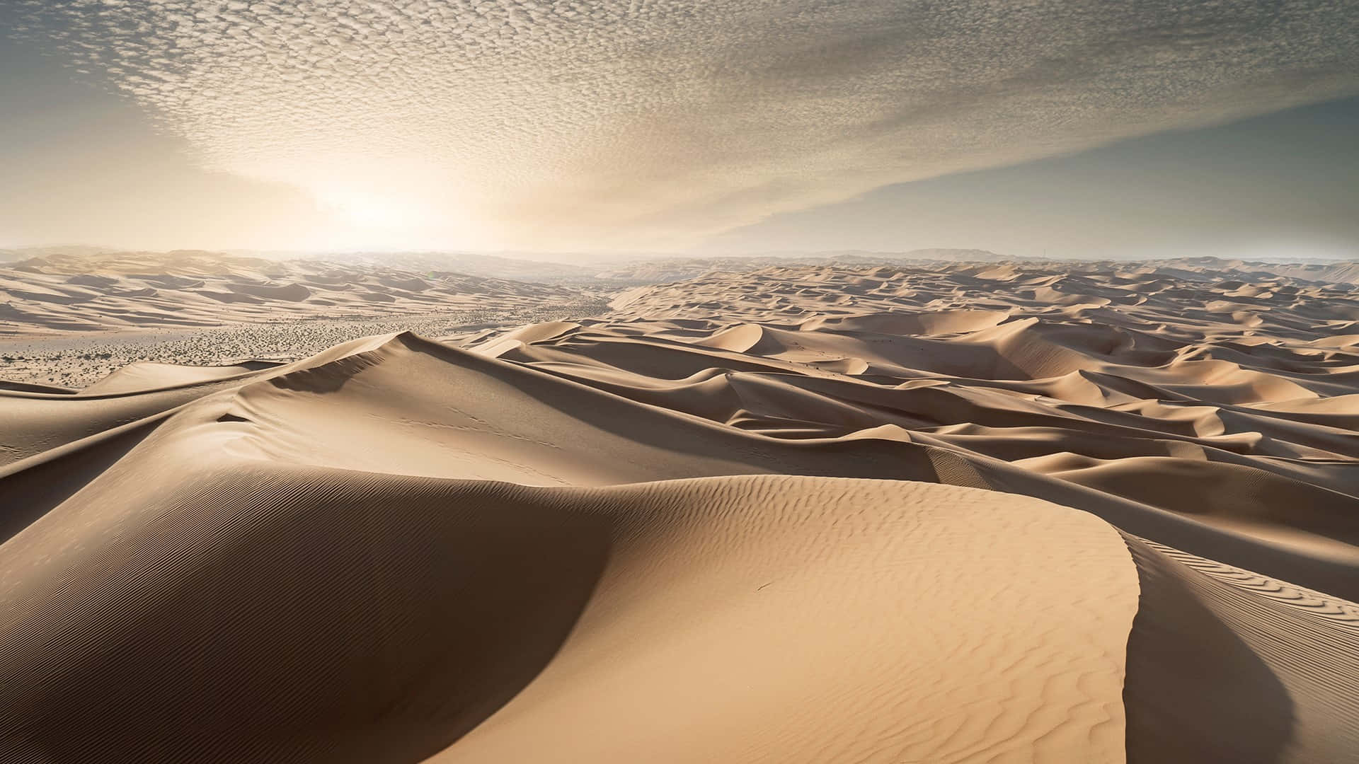 Sand Dunes 桌布 壁紙 — 廣闊的金色沙丘在紋理天空下延伸，太陽在無盡的沙漠地平線上升起。