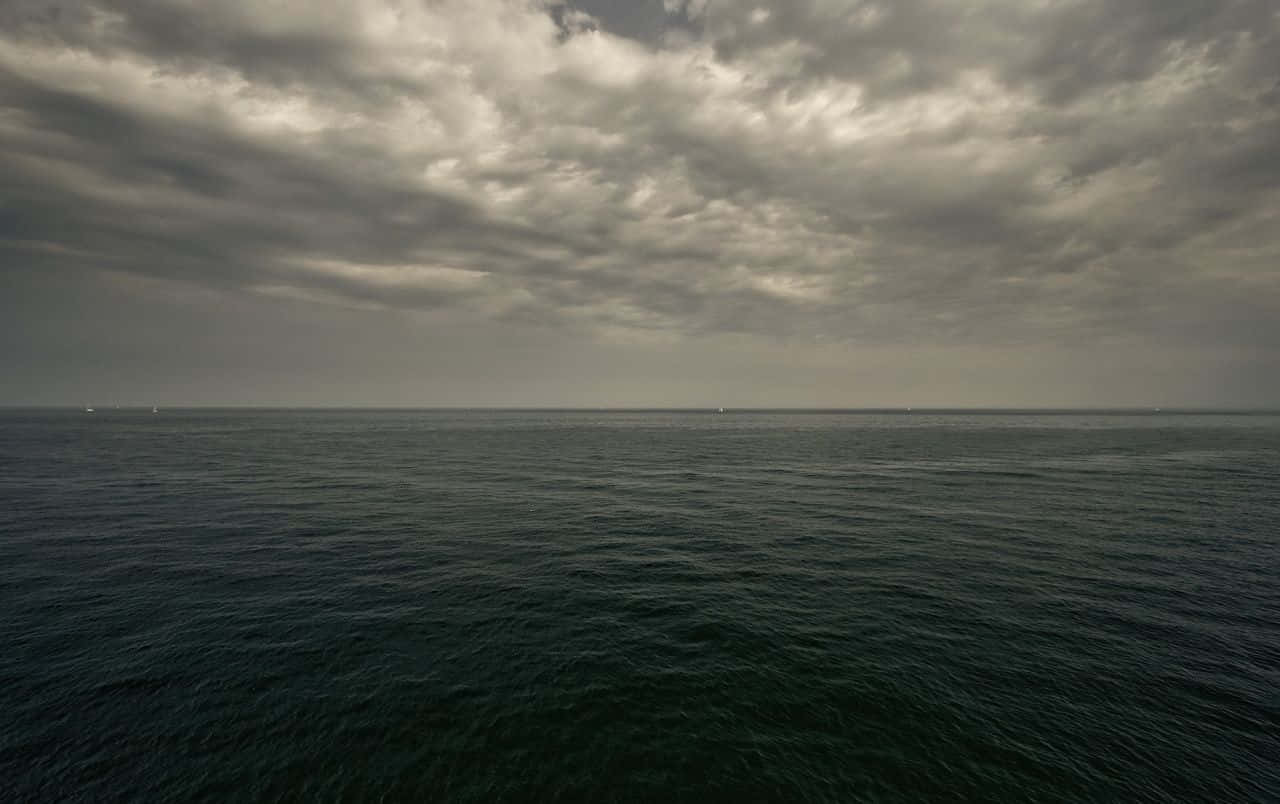 Dark Ocean 桌布 壁紙 — 廣闊的黑暗海洋在沉重的陰天下延伸，遠方的船隻在地平線上幾乎看不見。