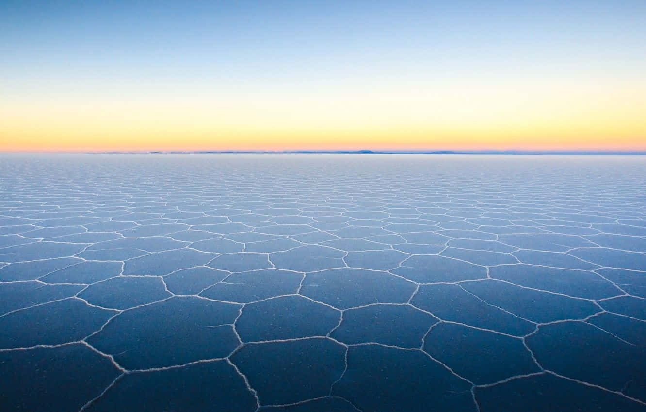 Frozen Lake 桌布 壁紙 — 廣闊的龜裂鹽灘在柔和的金色與藍色日出色調下延伸至地平線。