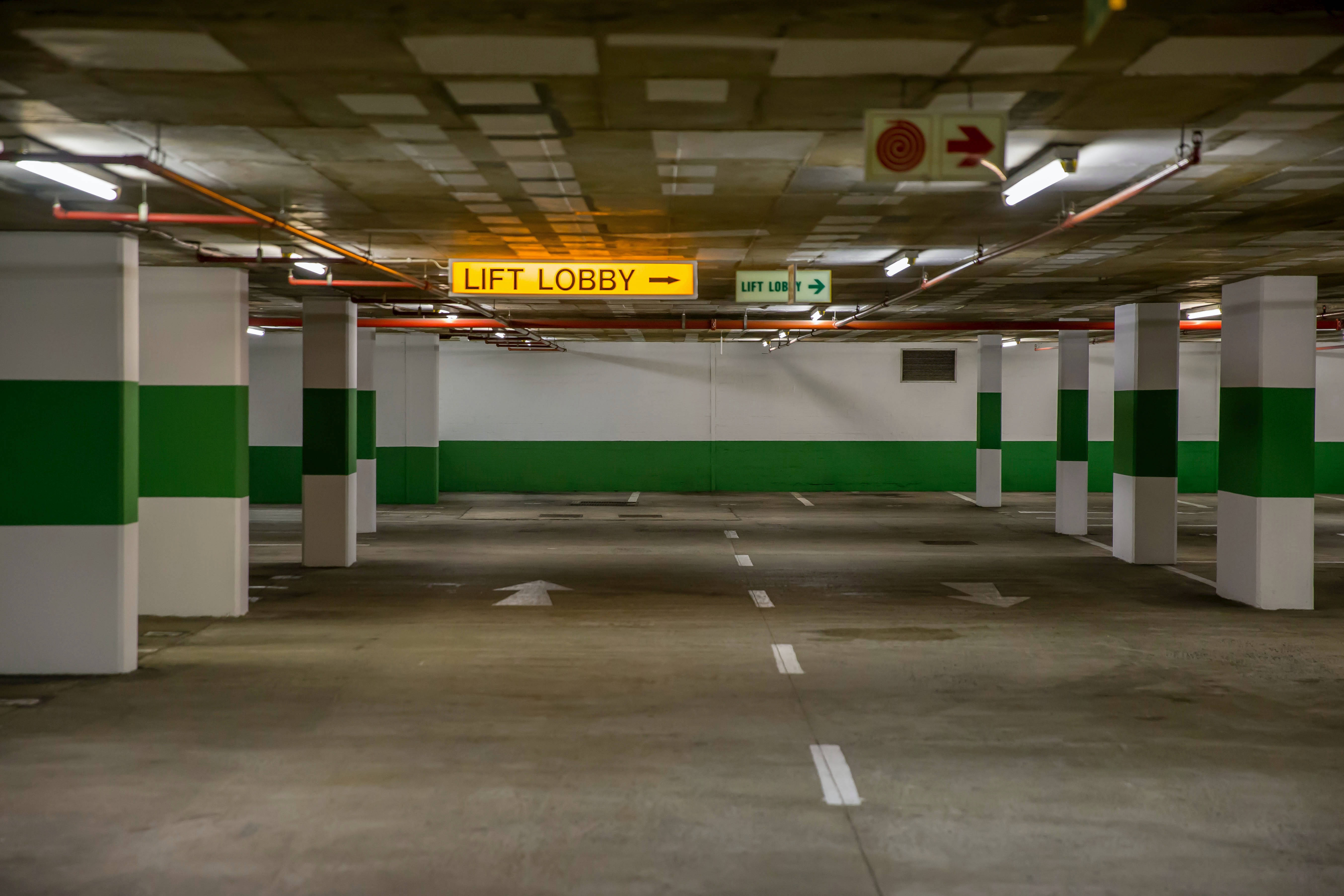 廣闊空曠的地下停車場 壁紙 — 一個空的地下停車場，有綠色和白色的柱子以及通往電梯大堂的照明方向標誌。