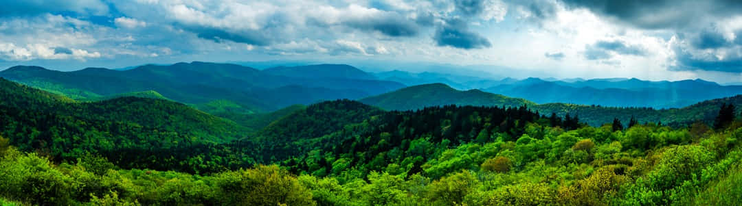Blue Ridge Mountains 桌布 壁紙 — 廣闊起伏的山脈，覆蓋著茂密的綠色森林，在戲劇性的多雲天空下。