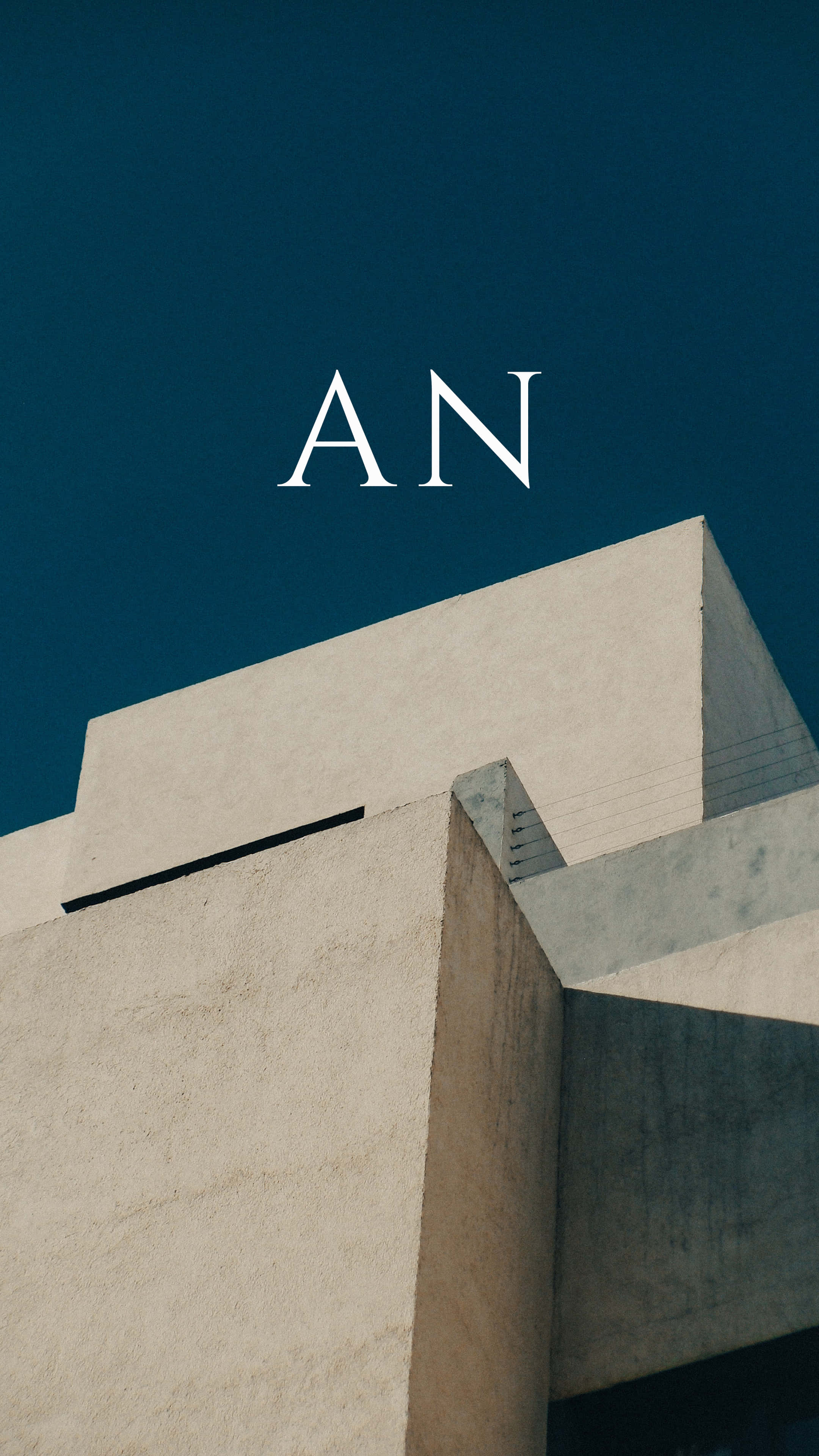 建築上方的「AN」字樣 壁紙 — 大膽的白色字母AN漂浮在鮮明的幾何混凝土建築之上，背景是深藍綠色天空。