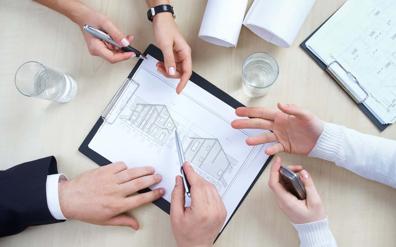 Four people reviewing architectural blueprints at a desk during a business meeting.