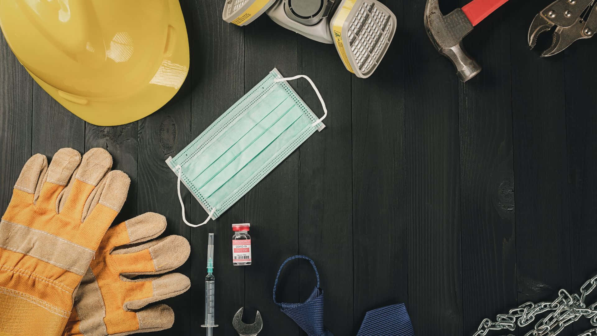 Labor Day 桌布 壁紙 — 建築工具和醫療物品（如口罩和疫苗瓶）排列在深色木質表面上。