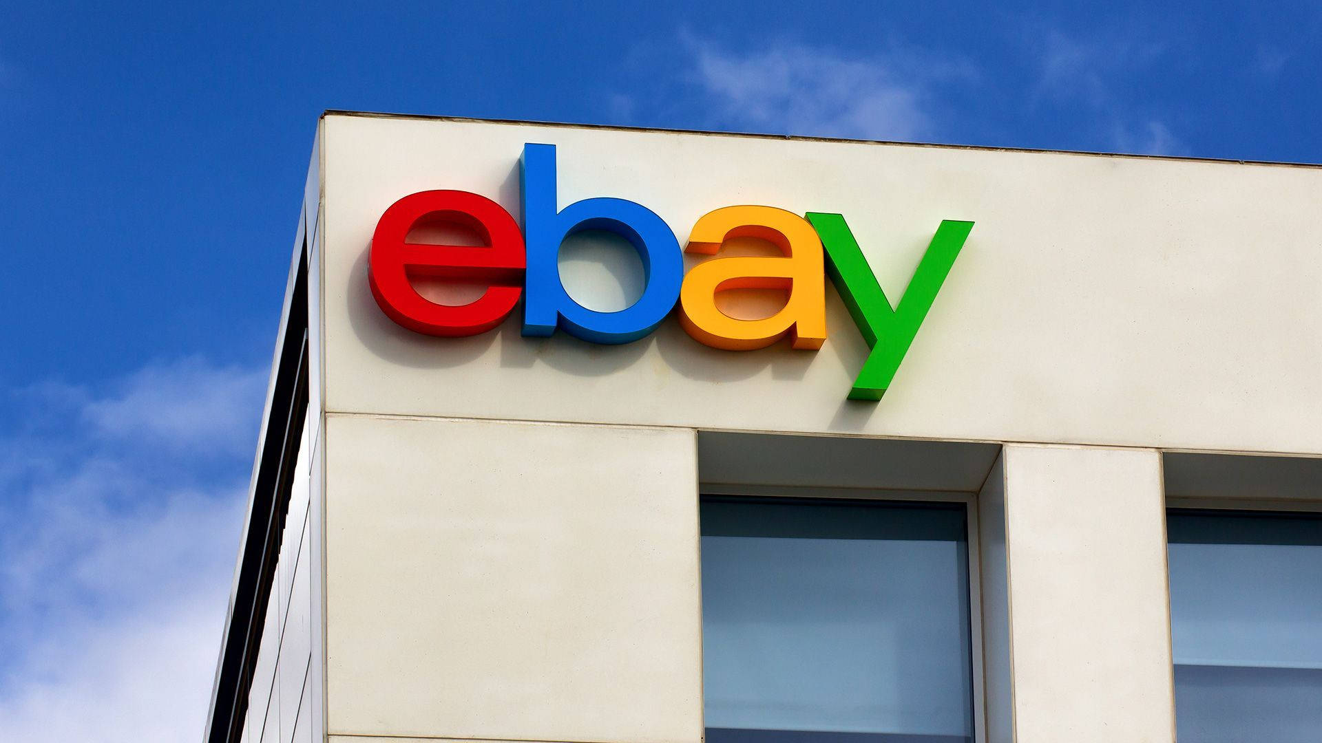建築物上的 eBay 標誌 壁紙 — 鮮豔的eBay標誌，以紅、藍、黃、綠色呈現，安裝在現代建築上，背景是清澈的藍天。