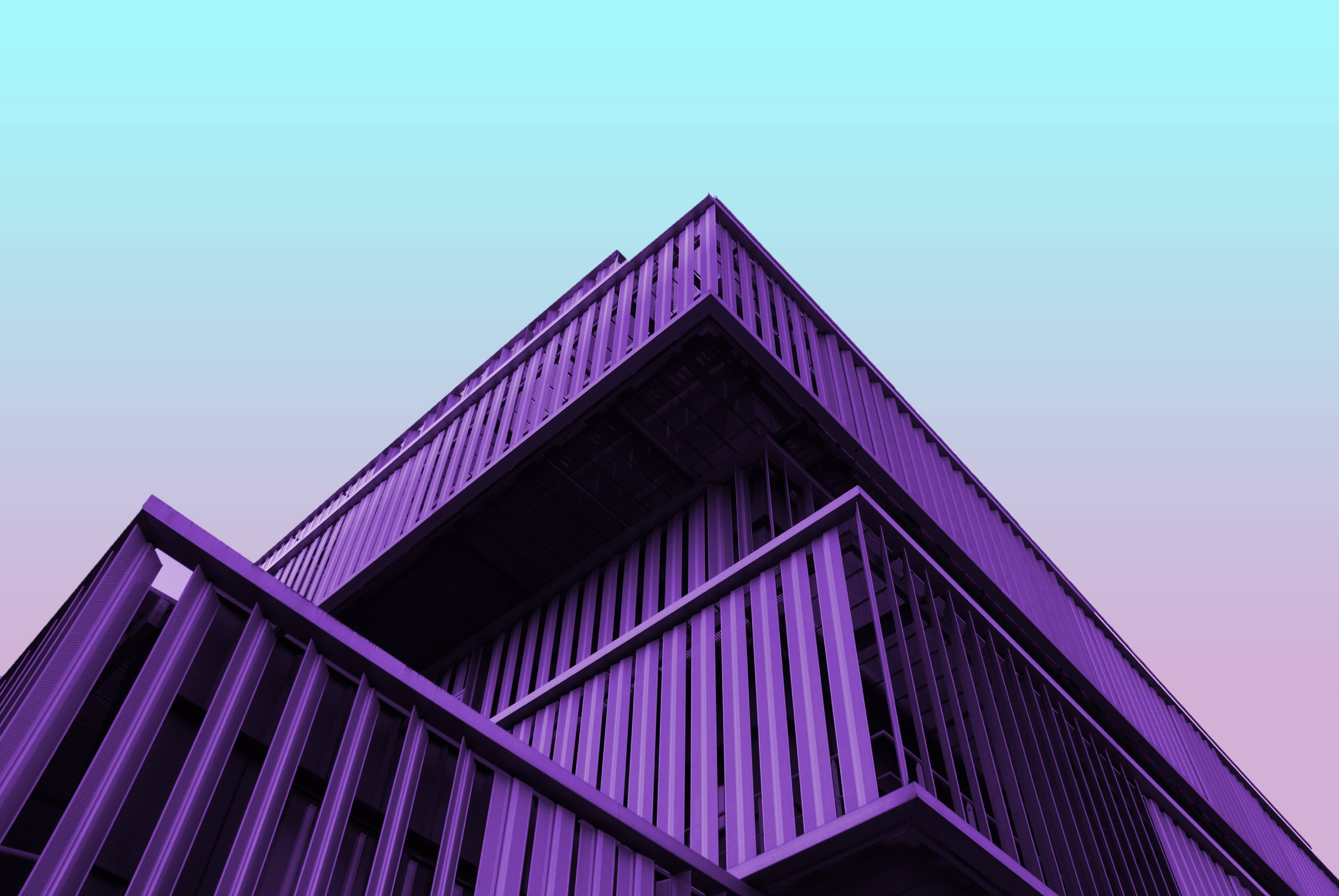 建築紫色美學 壁紙 — 低角度拍攝的現代幾何建築，帶有紫色金屬面板，背景是漸變天空。