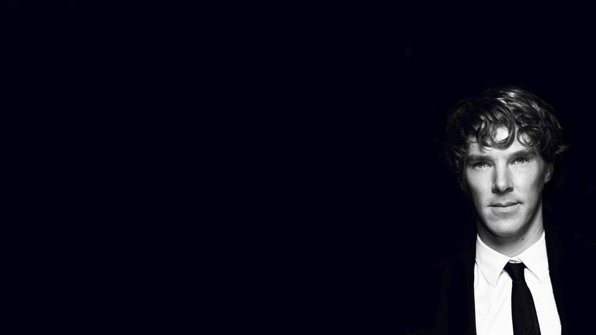 一個穿著西裝打領帶的男人在黑暗的攝影棚中直視鏡頭。