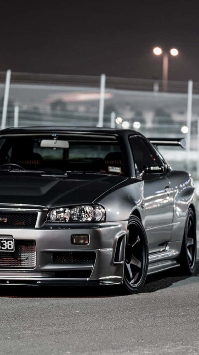 銀色日產Skyline GT-R在夜間停泊在賽車場上，在明亮的燈光下。
