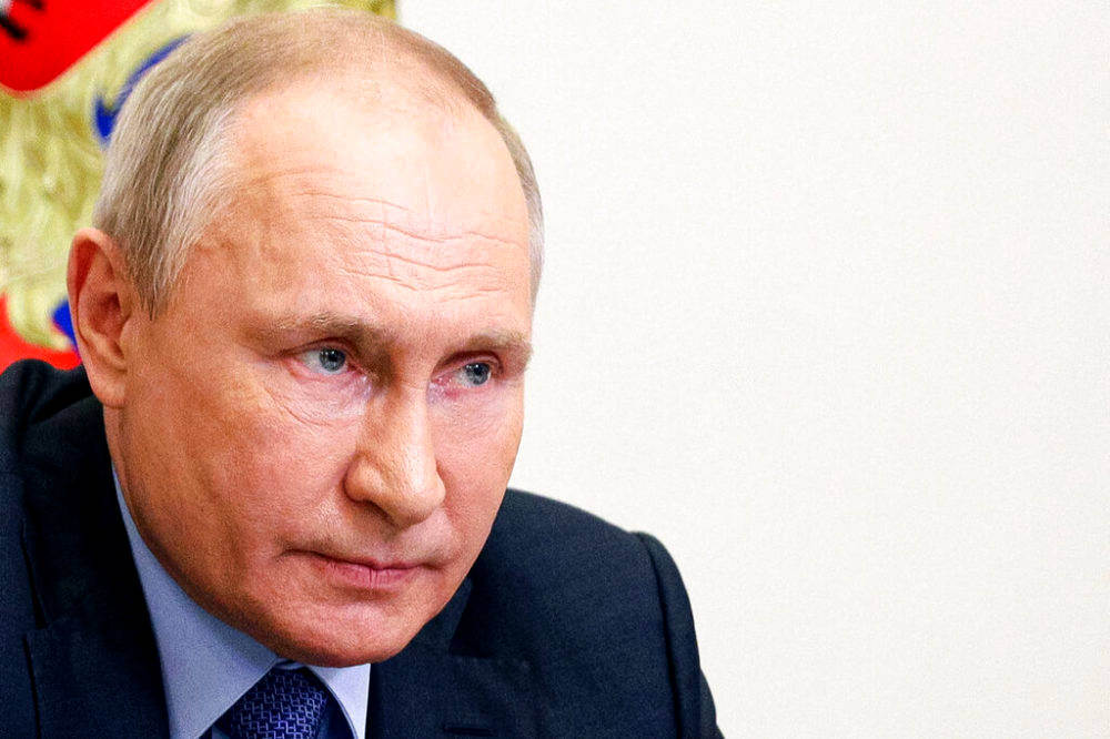 弗拉基米尔·普京的強烈凝視 壁紙 — 弗拉基米爾·普京的頭像特寫，身穿深色西裝和藍色領帶，背景為白色牆壁，身後可見部分俄羅斯國徽。