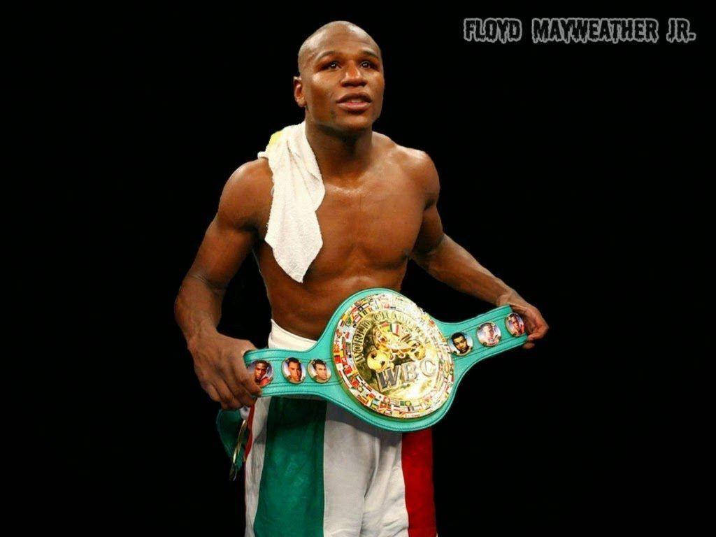 弗洛伊德·梅威瑟戴上冠軍腰帶 壁紙 — 弗洛伊德·梅威瑟（Floyd Mayweather Jr.）自信地站在黑色背景前，肩上搭著毛巾，手持WBC拳擊冠軍腰帶。