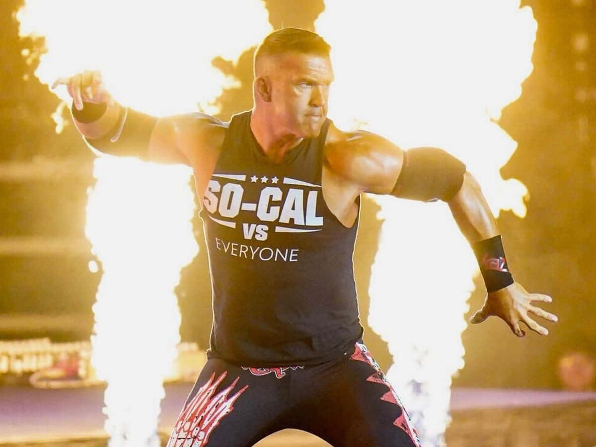 身穿印有「SO-CAL VS EVERYONE」黑色背心的摔角手，被熾熱的爆炸包圍。