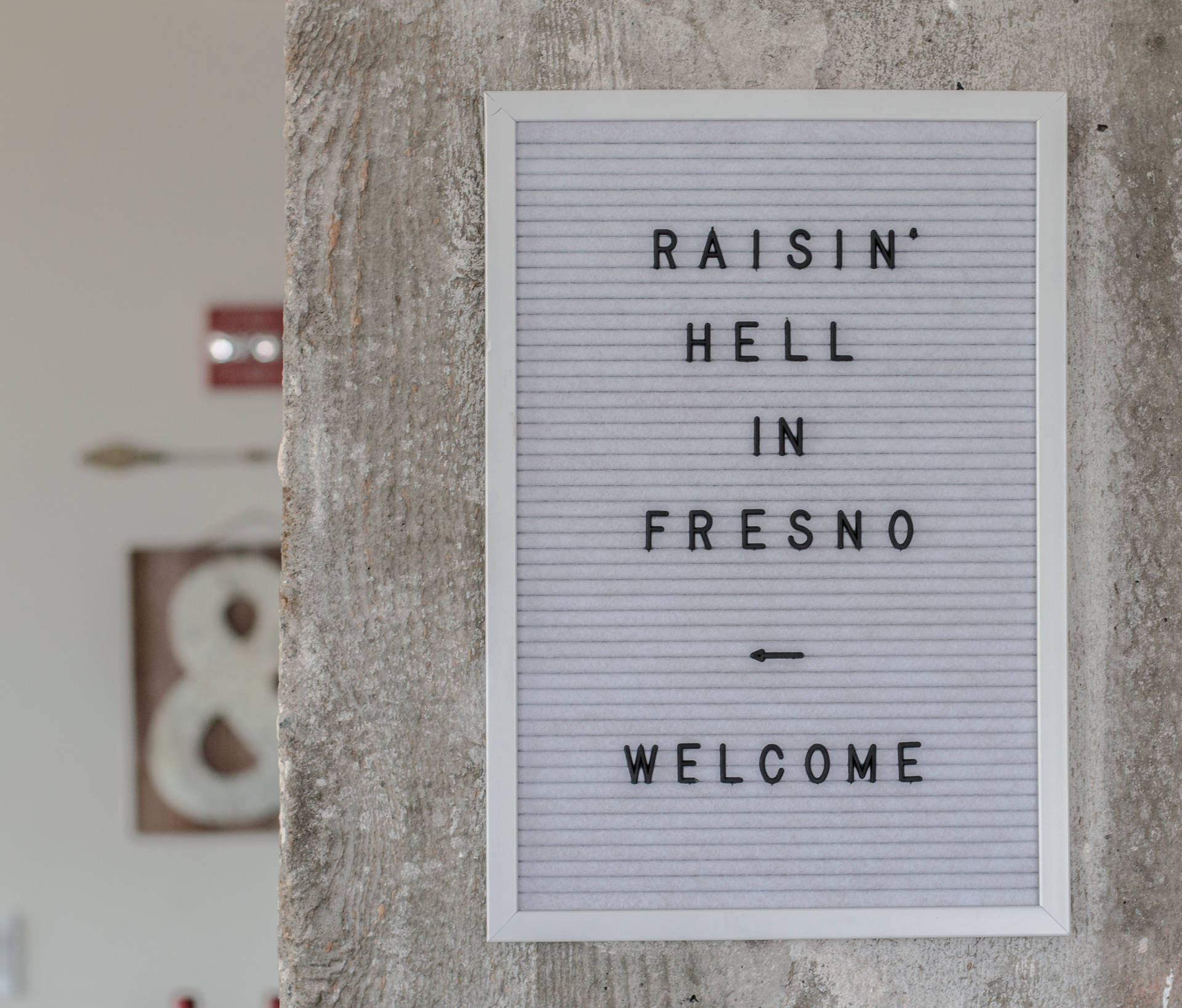 一個喺混凝土牆上嘅字母板標誌寫住 'Raisin' Hell in Fresno Welcome'，仲有一個箭嘴。