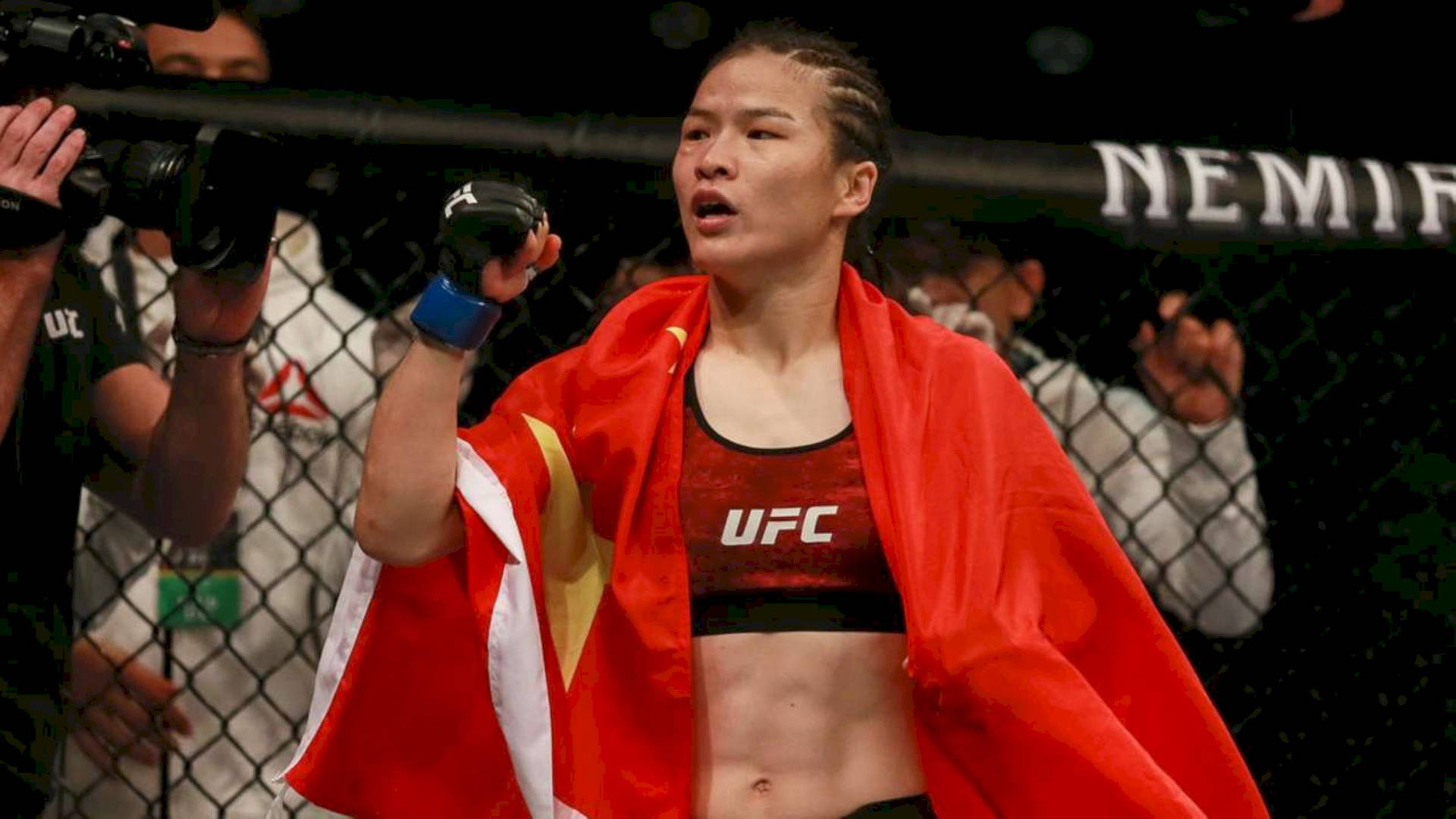 女MMA拳手披紅旗在UFC八角籠慶祝勝利。