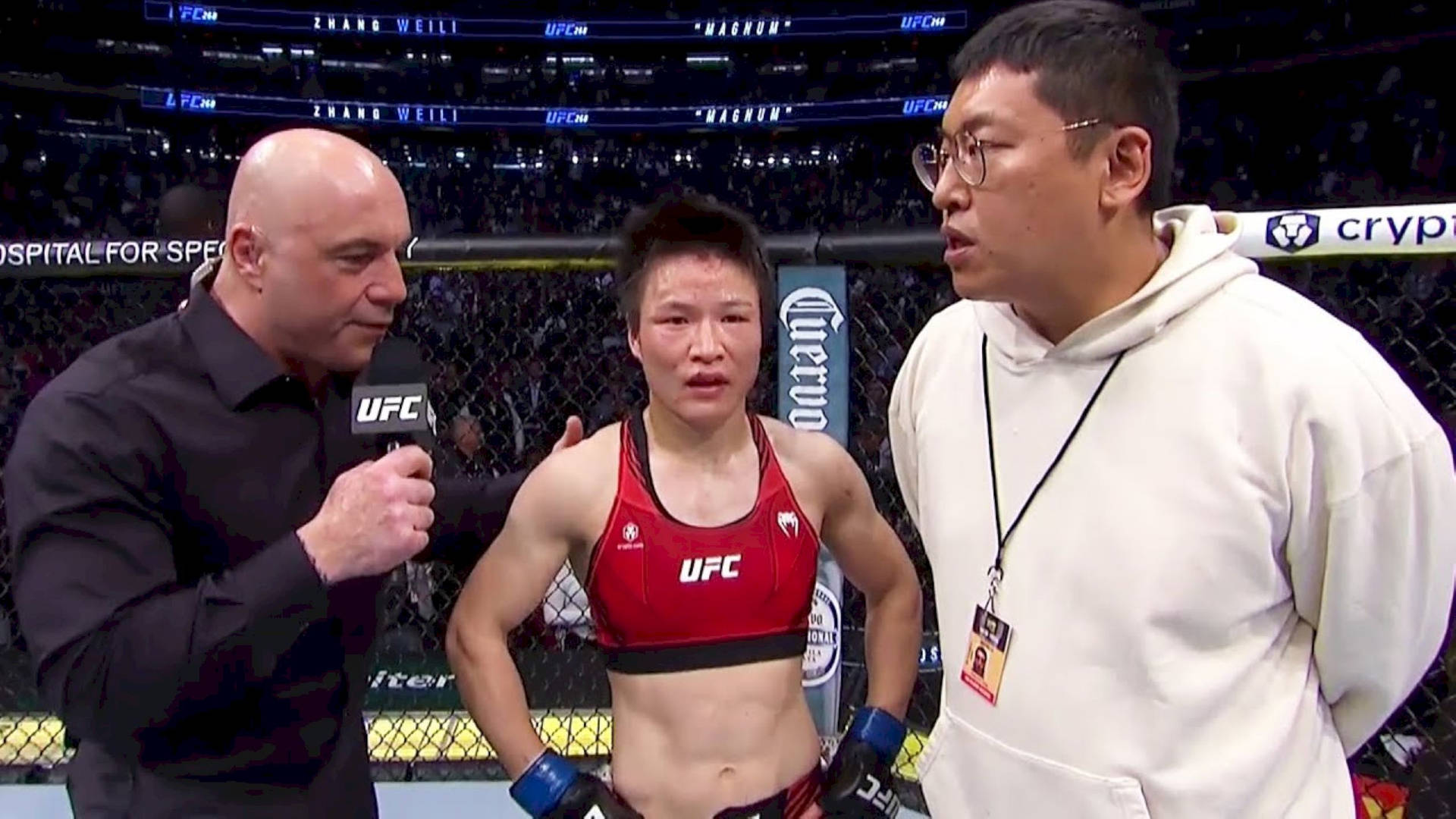 UFC拳手在八角籠內接受訪問，旁邊有一位身穿白色連帽衫的男子。
