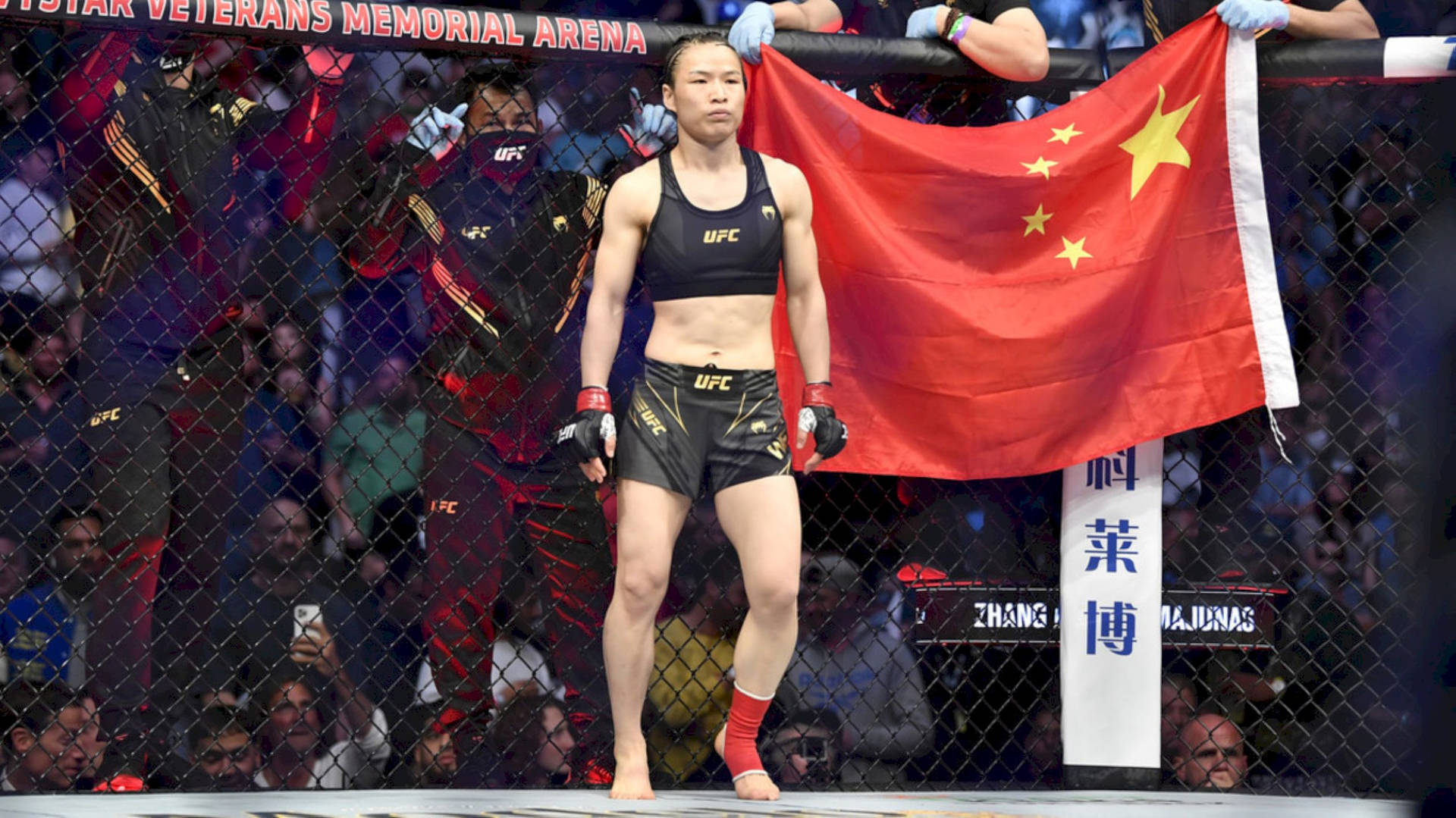 女性MMA拳手在UFC八角籠中手持中國國旗，觀眾觀看。