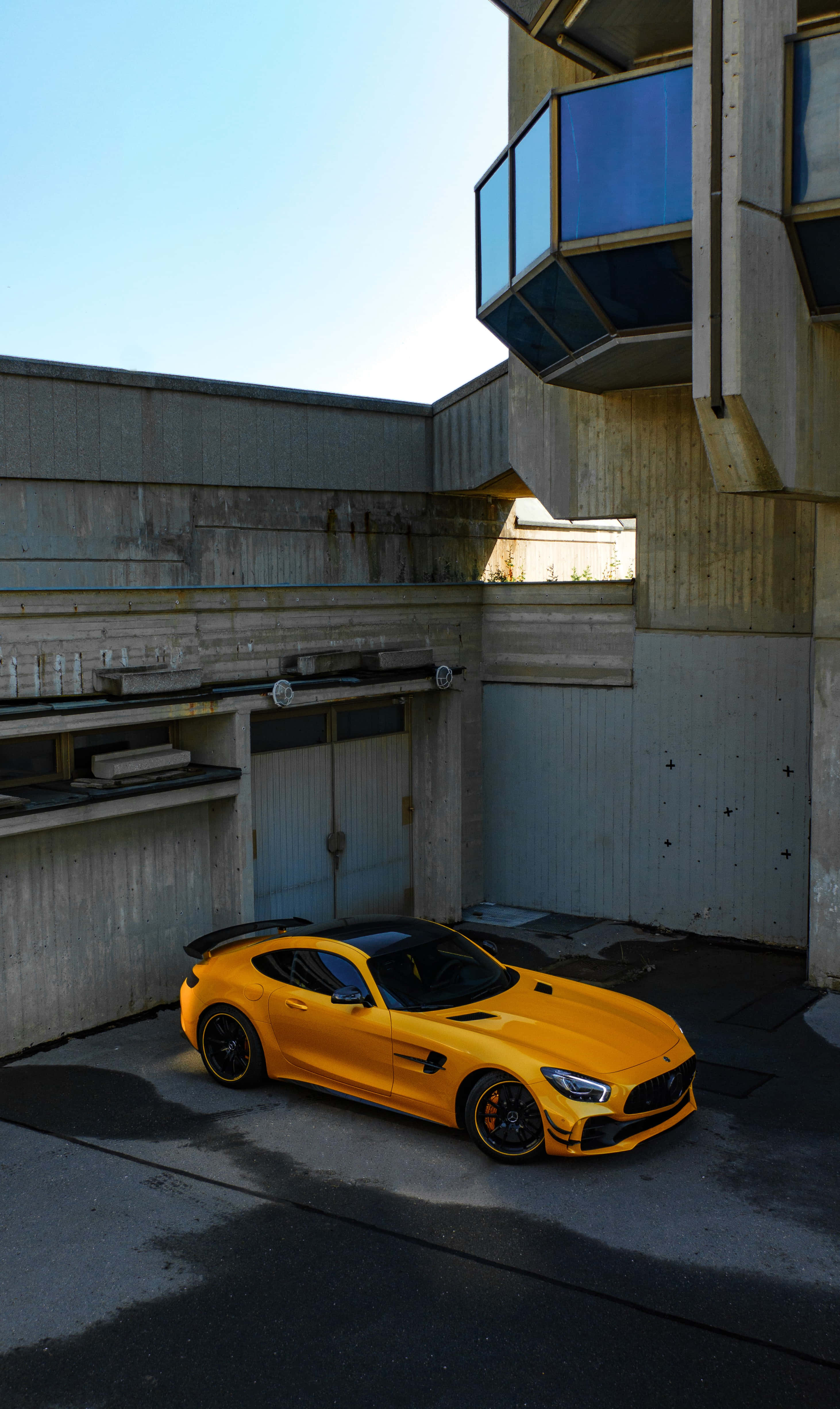 強勁AMG GT-R於鮮豔背景 壁紙 — 一輛充滿活力的黃色跑車停放在現代混凝土庭院中，上方是清澈的藍天。
