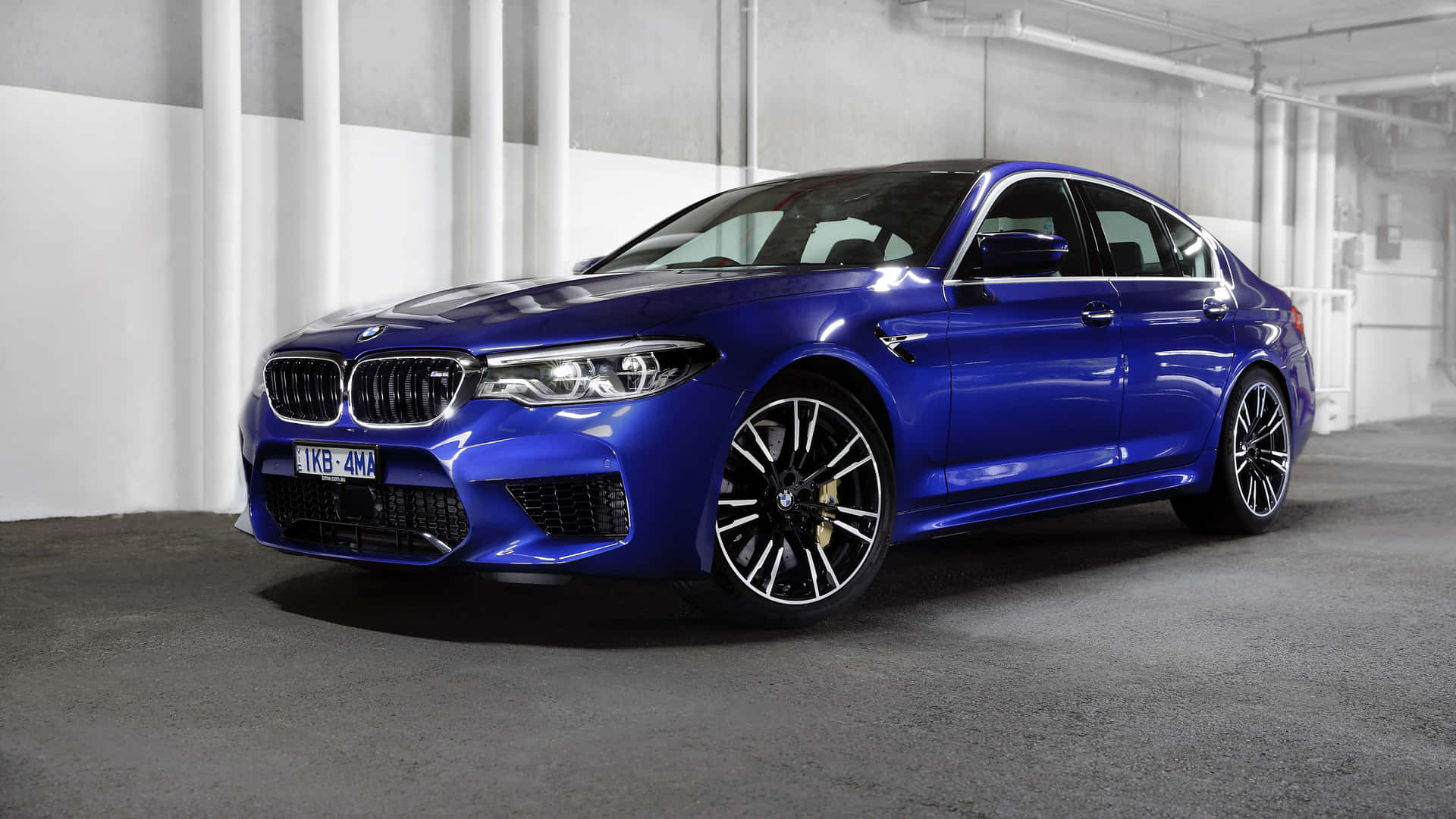 光澤的藍色BMW M5房車停在一個混凝土車庫中，帶有白色柱子。