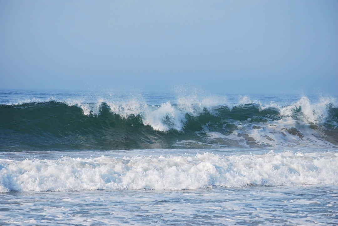 Beach Waves 桌布 壁紙 — 強勁的海浪帶著白色泡沫，在明亮的日光下拍打著朦朧的藍天。