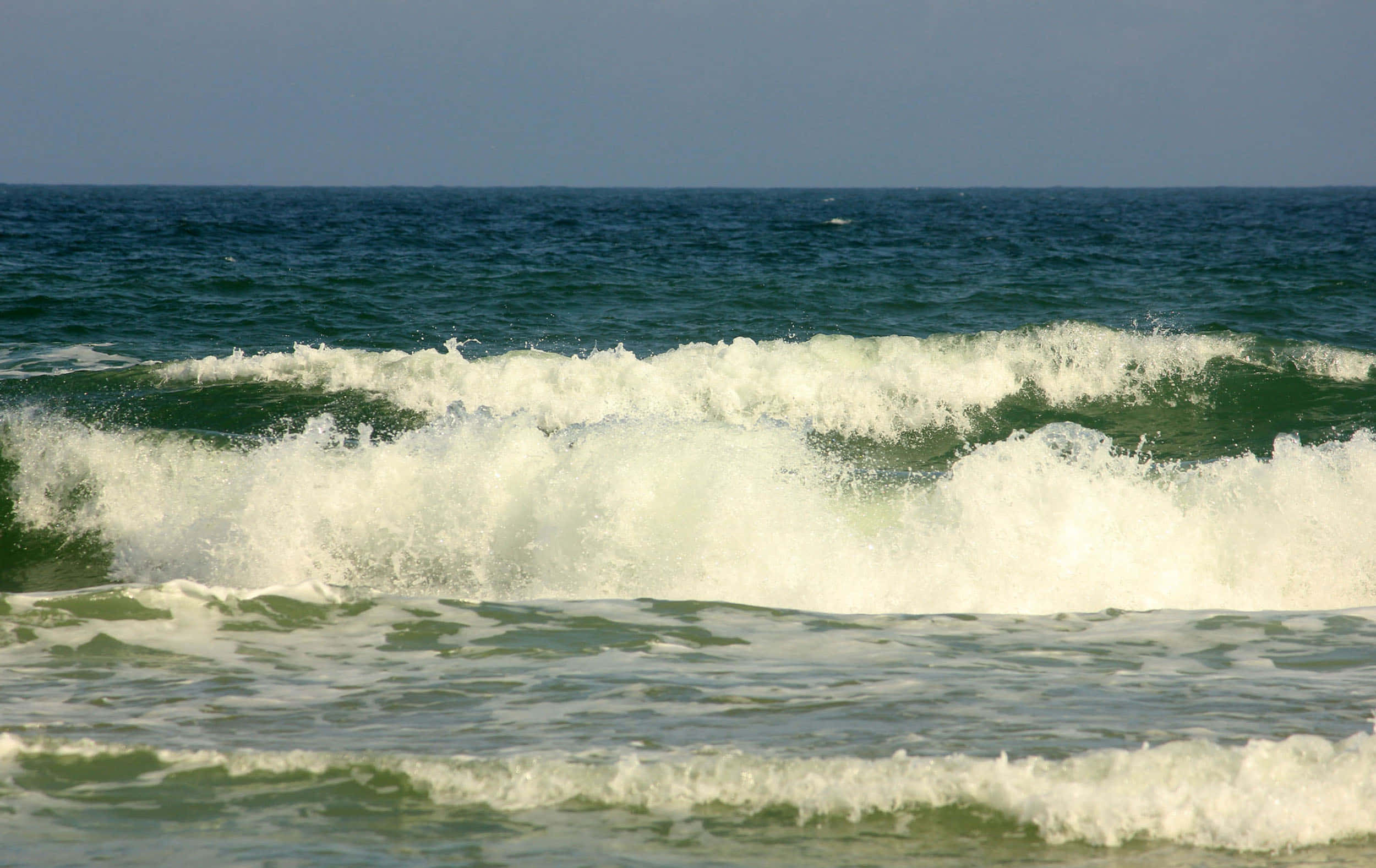 Beach Waves 桌布 壁紙 — 強勁的海浪帶著白色泡沫拍打著晴朗天空下平靜的藍色大海。