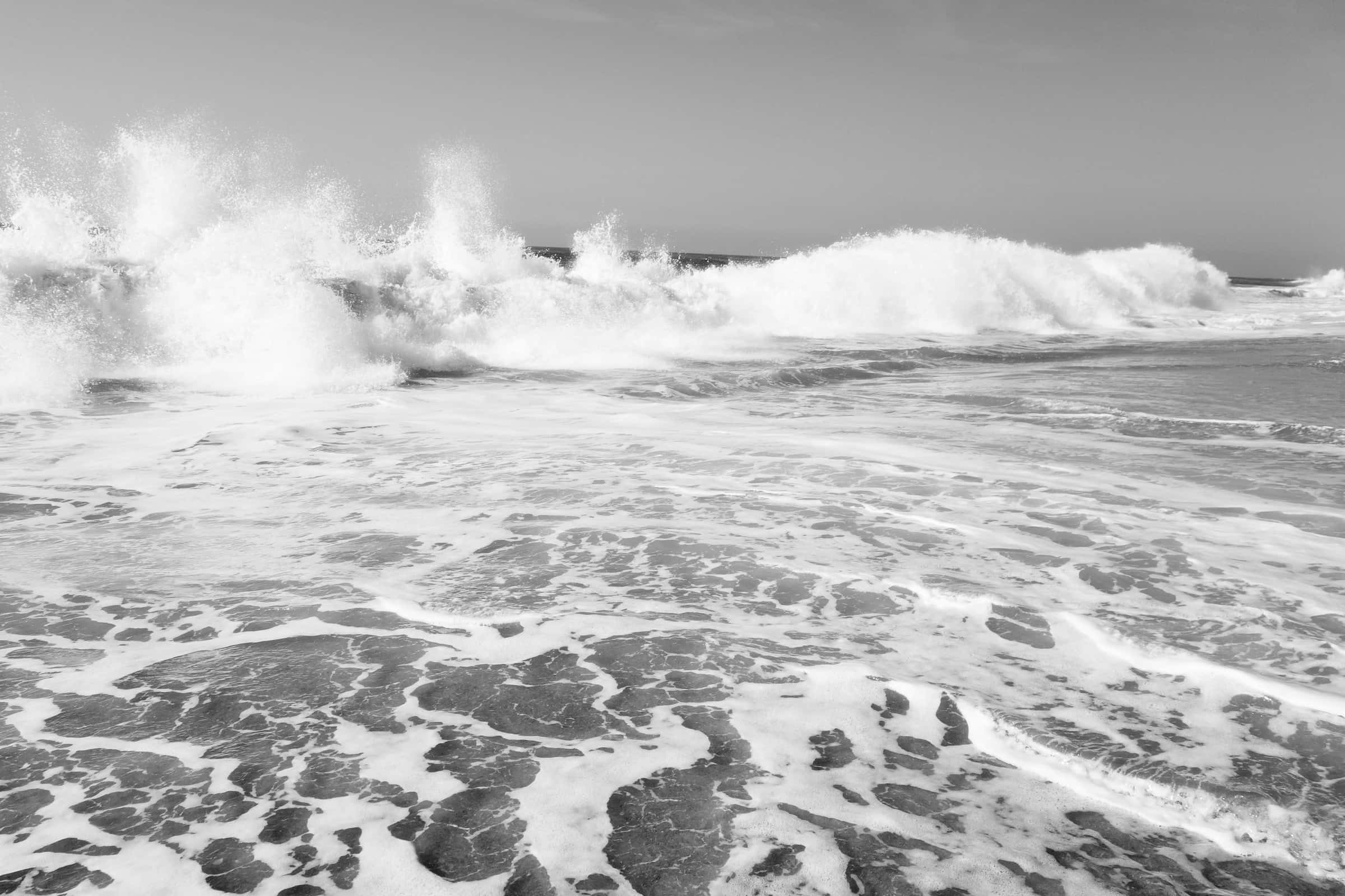 Black And White Beach 桌布 壁紙 — 強勁的海浪拍打，在單色調的海岸線上形成戲劇性的白色泡沫。
