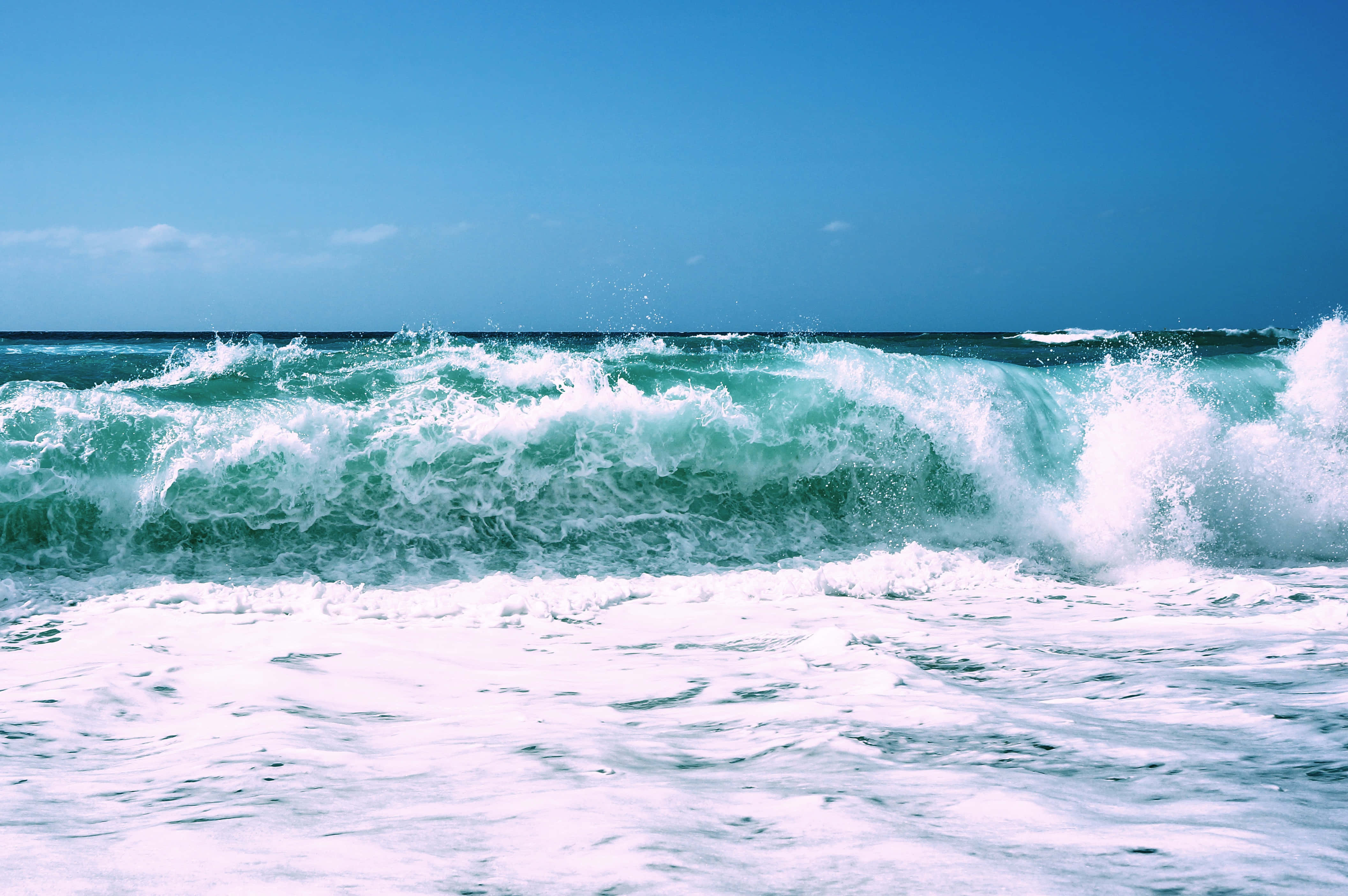 Beach Waves 桌布 壁紙 — 強勁的藍綠色海浪帶著白色泡沫拍打著清澈的藍天。