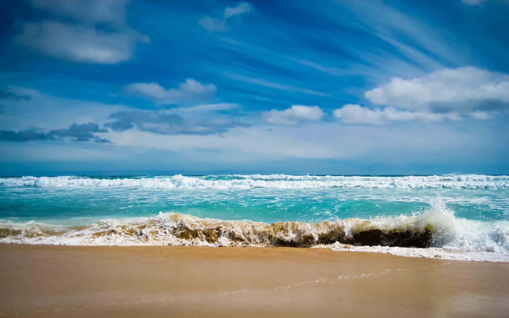 Beach Desktop 桌布 壁紙 — 強勁的藍綠色海浪拍打著金色沙灘，上方是湛藍的天空，點綴著蓬鬆的白雲。