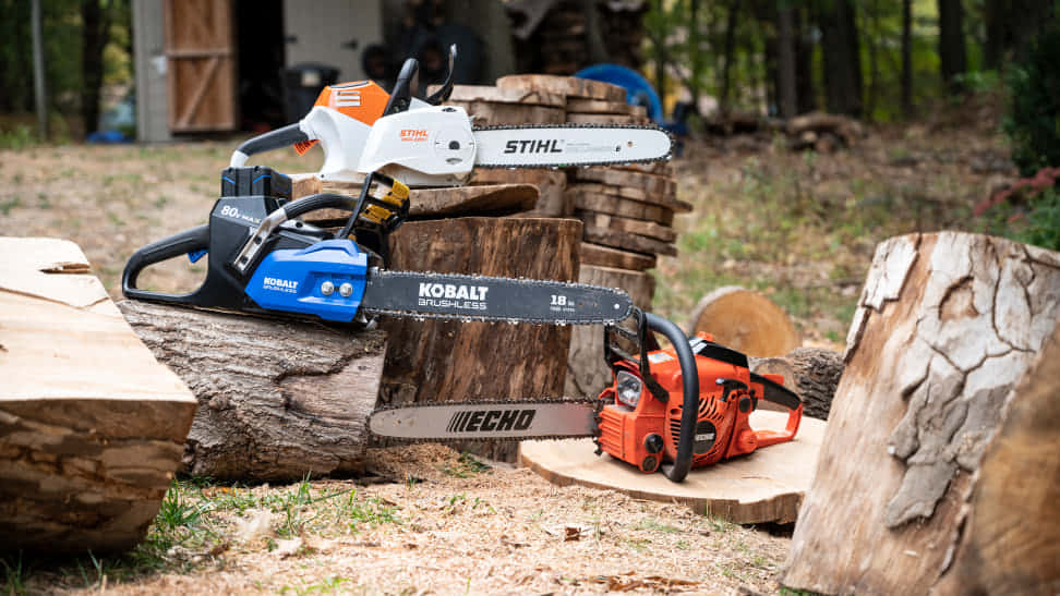 強勁耐用的電鋸 壁紙 — 三把來自STIHL、Kobalt和Echo品牌的鏈鋸，放置在樹林戶外工作環境中剛砍伐的木頭上。