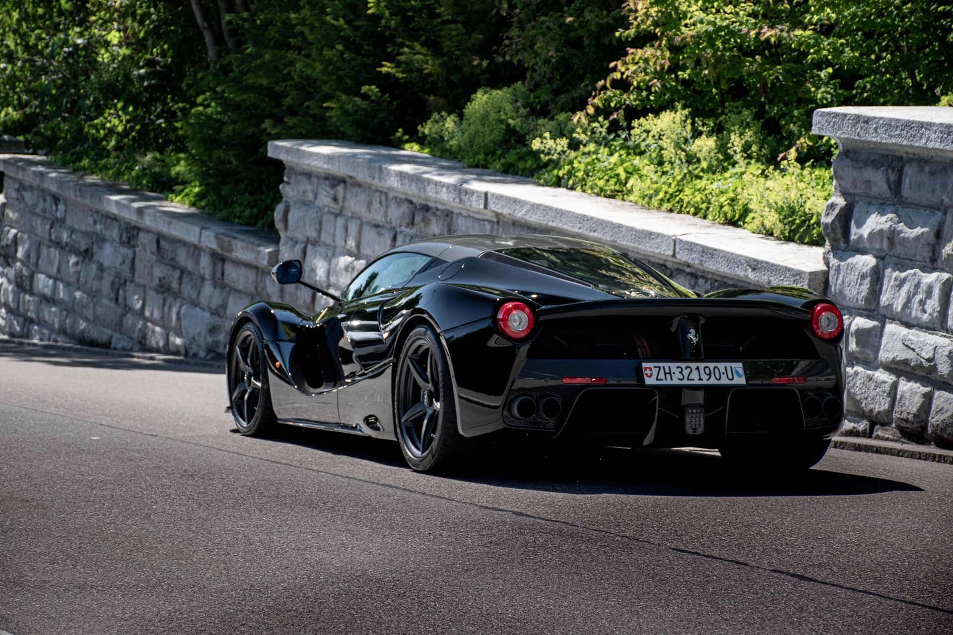 黑色法拉利 LaFerrari 在蜿蜒的山路上，有石牆和綠樹。