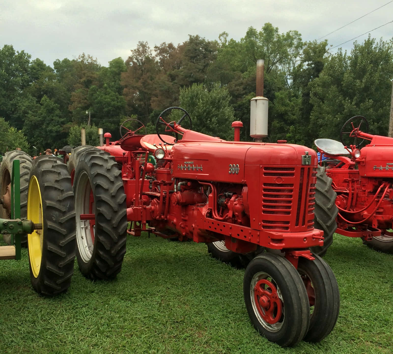 強勁農業拖拉機在農場 壁紙 — 復古紅色 Farmall 拖拉機配黃色輪胎，停泊在陰天下的綠色草地上。