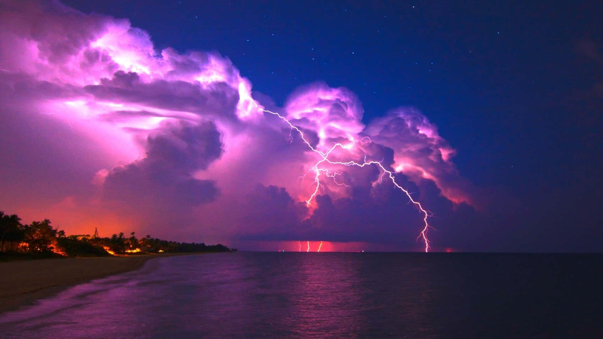 強勁閃電照亮繁星夜空 壁紙 — 一場戲劇性的紫色雷暴照亮了夜晚的黑暗海洋，伴隨著發光的雲層和遠處的海岸燈光。