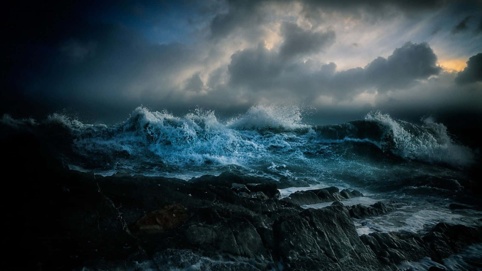 Dark Ocean 桌布 壁紙 — 強大的海浪在暴風雨黃昏的天空下，伴隨著戲劇性的雲層照明，衝擊著黑暗的鋸齒狀岩石。
