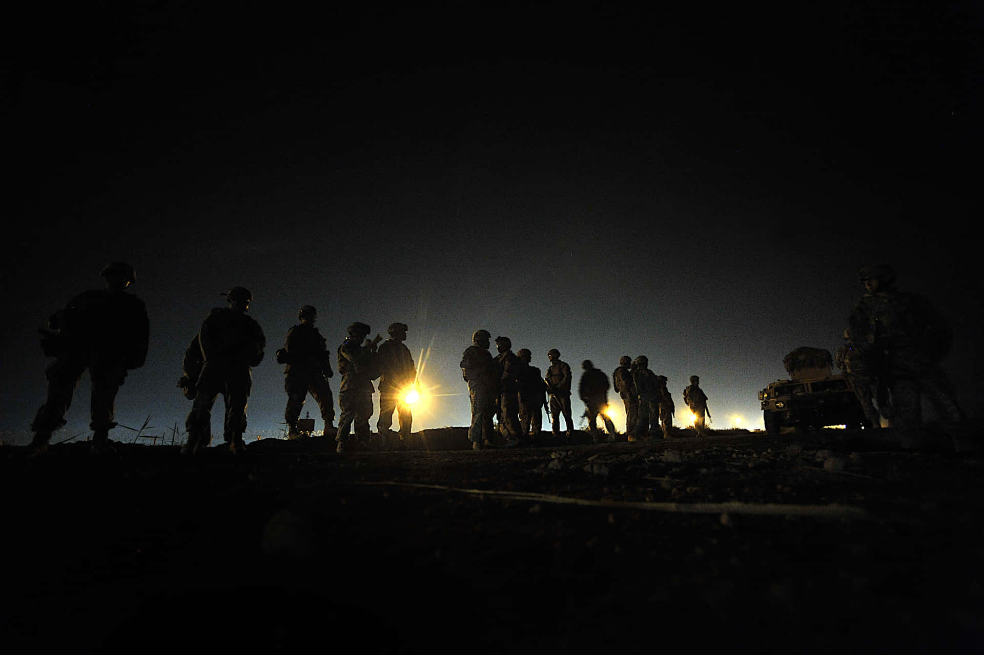 剪影士兵在夜間聚集在軍用車輛附近的燈光周圍。