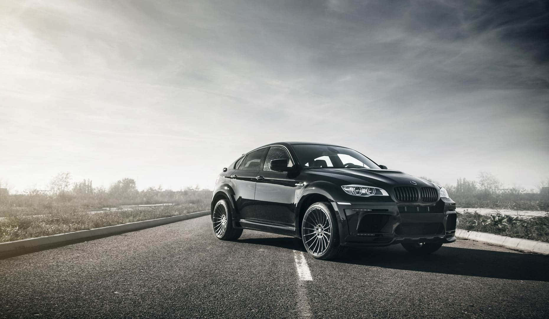 強悍有力：BMW X6 M 壁紙 — 一架時尚黑色BMW X6 M跑車停泊在陰天下空無一人的瀝青路上。