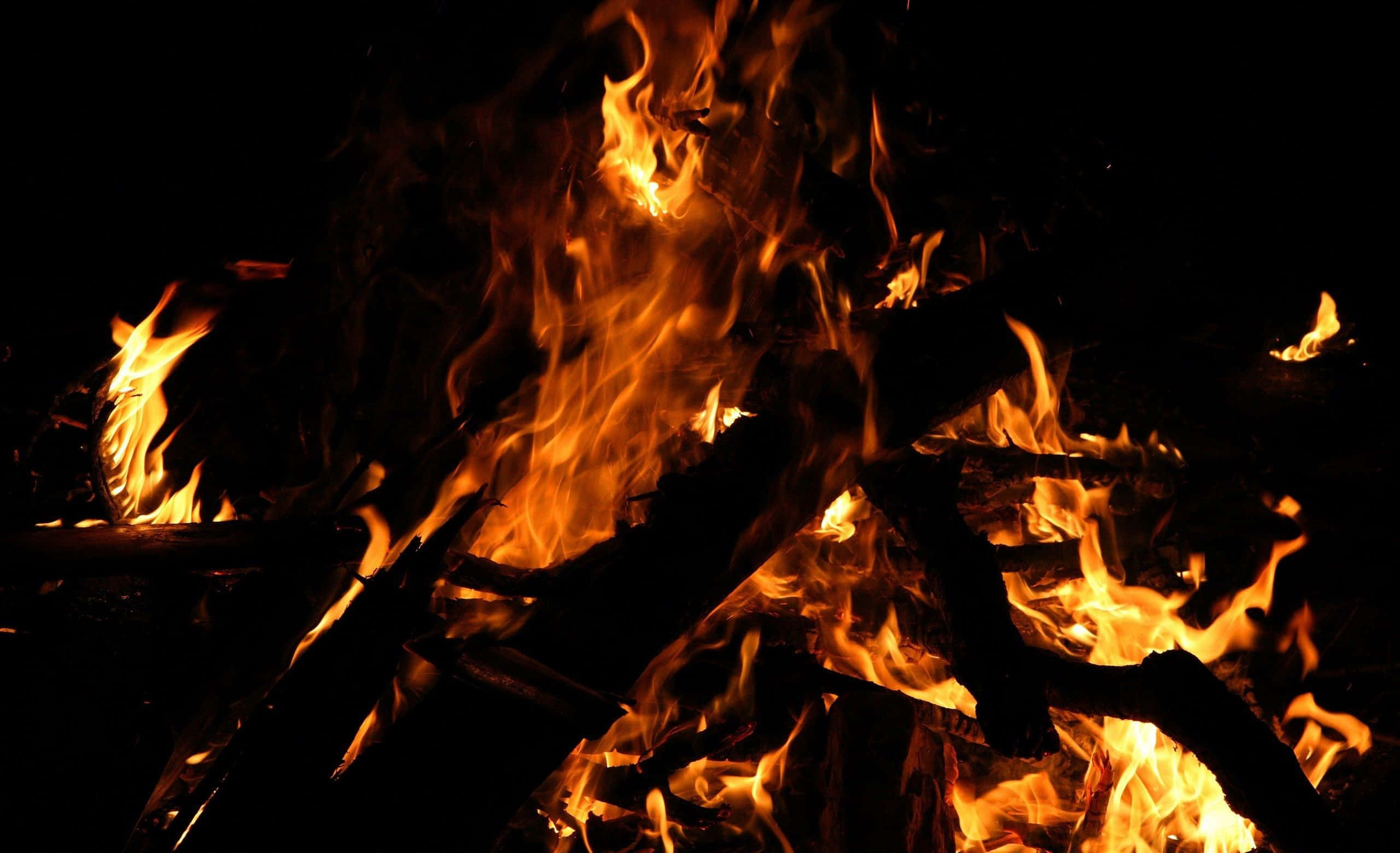 Beach Bonfire 桌布 壁紙 — 強烈的火焰在漆黑的夜空下，於焦黑的木頭上跳躍舞動。
