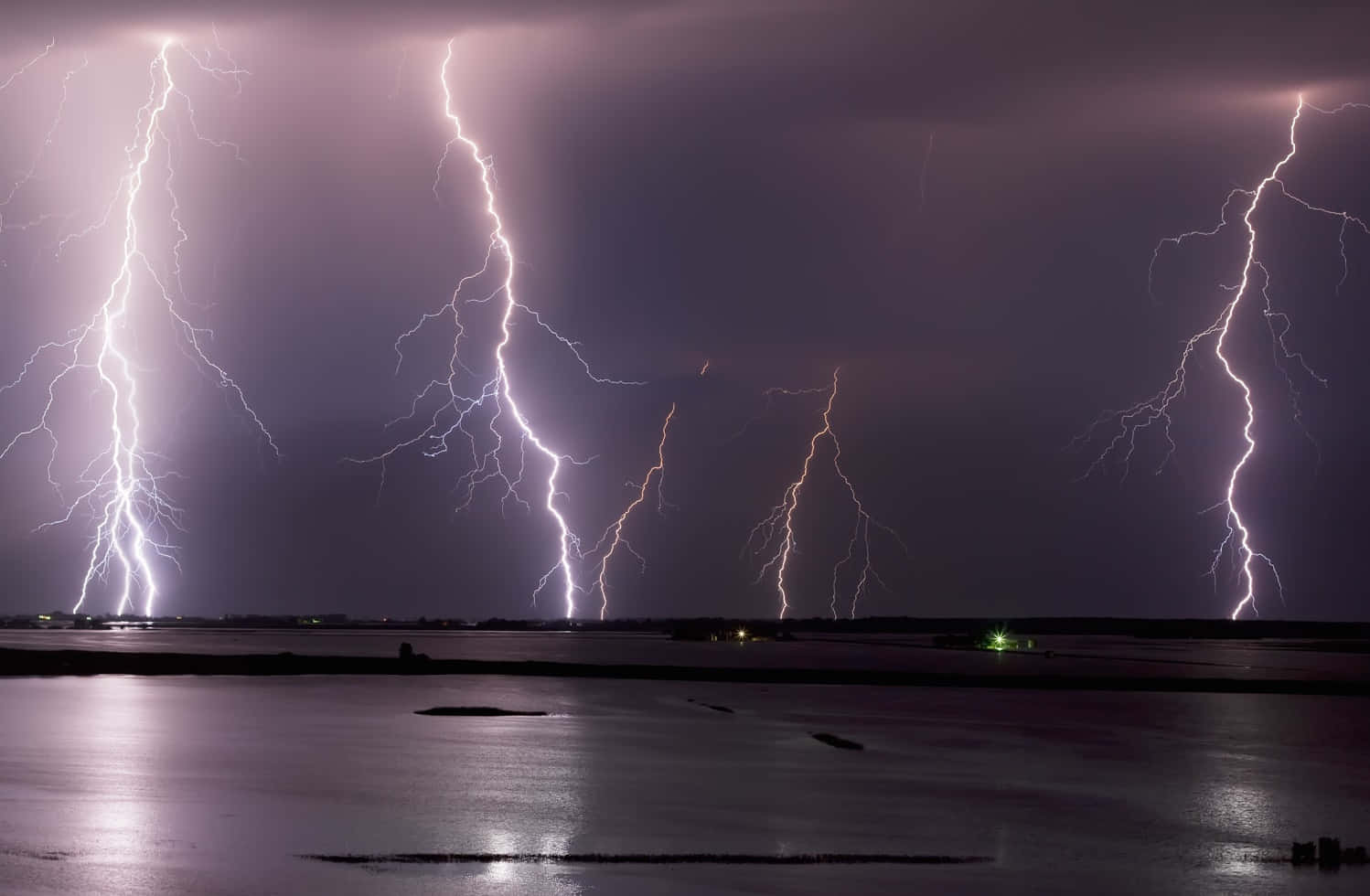 多道閃電照亮了夜晚平靜水面上方黑暗暴風雨的天空。
