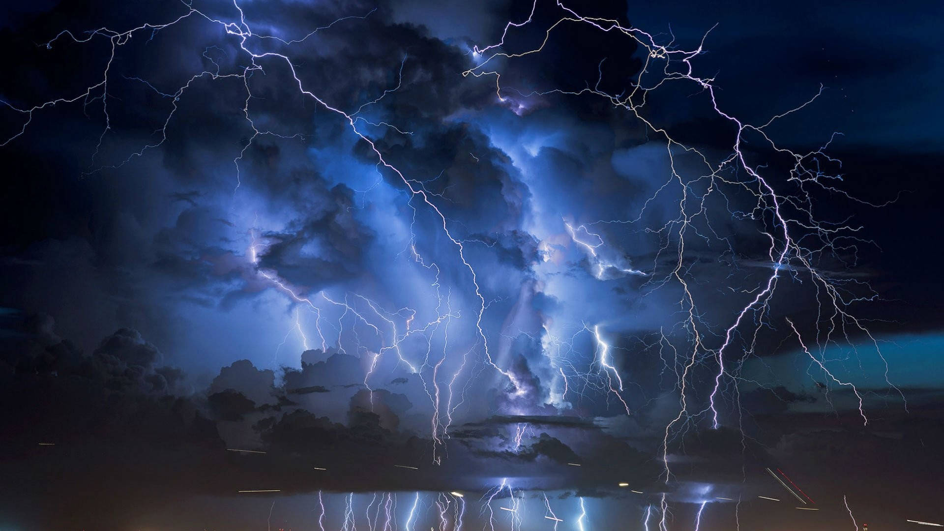 強烈雷暴最佳桌面壁紙 壁紙 — 強烈的閃電在暴風雨的夜空中劈啪作響，下方黑暗的水面反射出電光藍色的閃光。