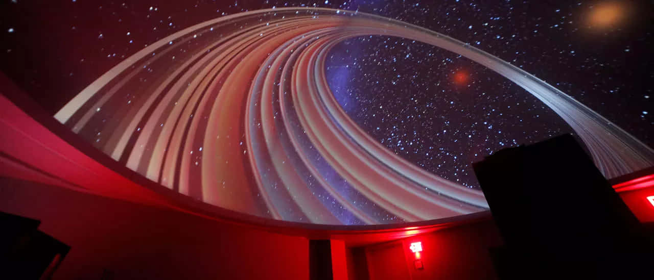 Planetarium 桌布 壁紙 — 彎曲的圓頂天花展示了一個漩渦星系投影，在黑暗背景下帶有星星和發光帶。