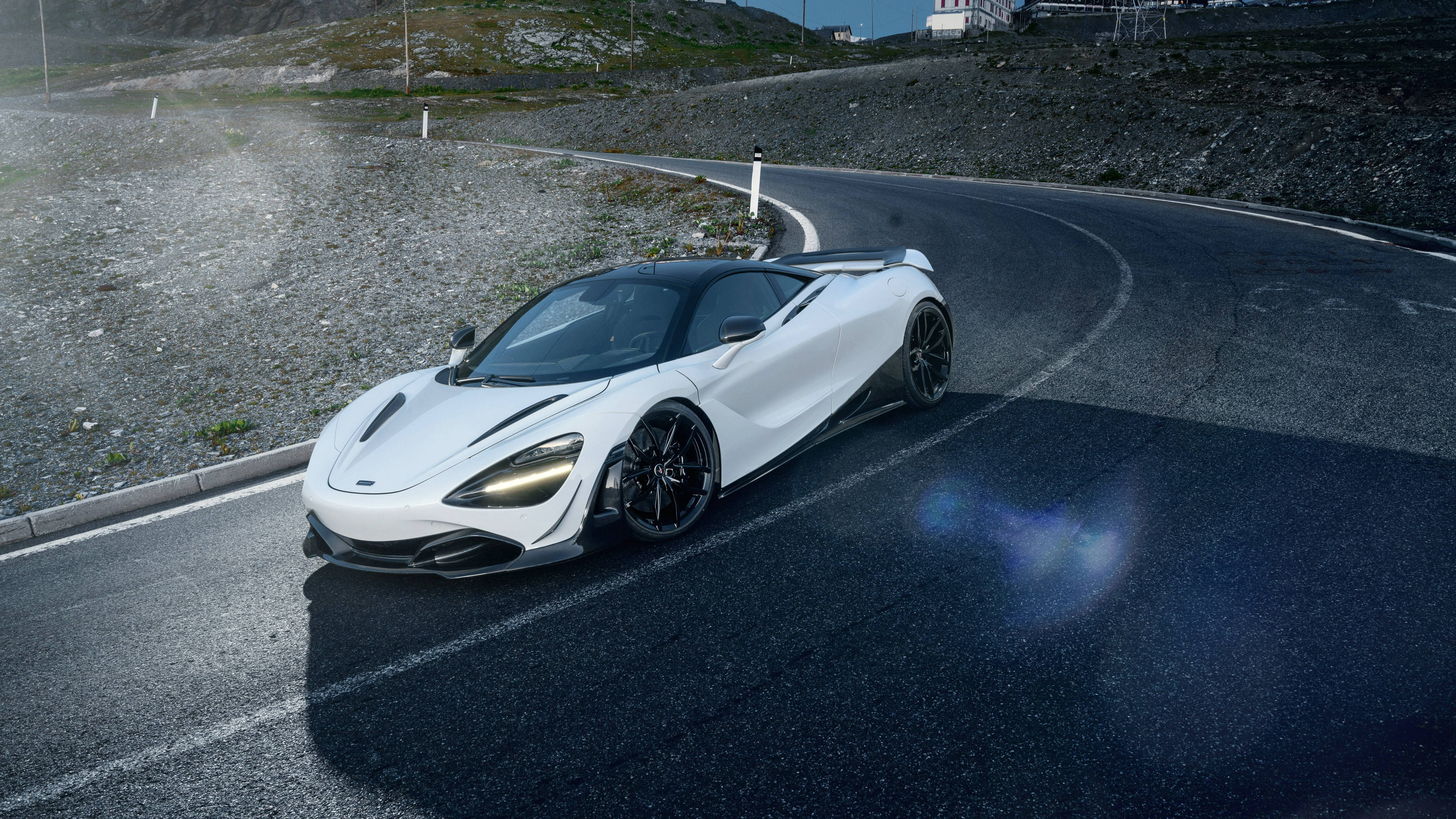彎道上的白色麥拉倫720S 壁紙 — 一輛時尚的白色McLaren跑車在晴朗的藍天下行駛在蜿蜒的山路上。