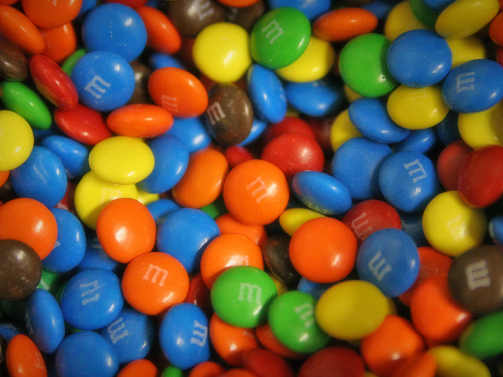 彩色M&M巧克力糖果 壁紙 — 各種色彩繽紛的M&M's糖果的鮮明特寫，帶有光澤外殼和白色「m」標誌。