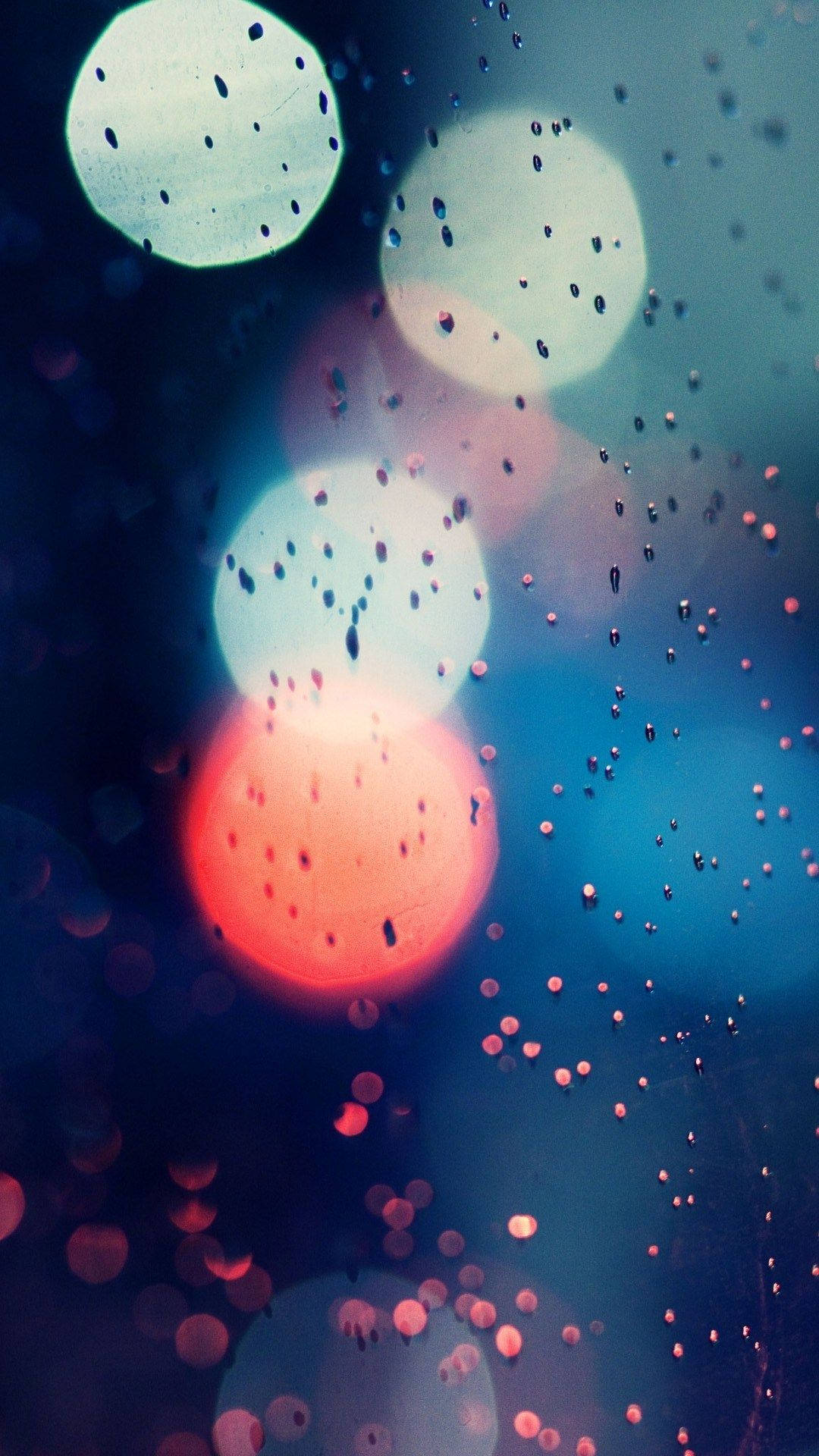 彩色光球與水滴手機壁紙 壁紙 — 玻璃上的雨滴將城市燈光模糊成柔和發光的紅色和藍色球體。