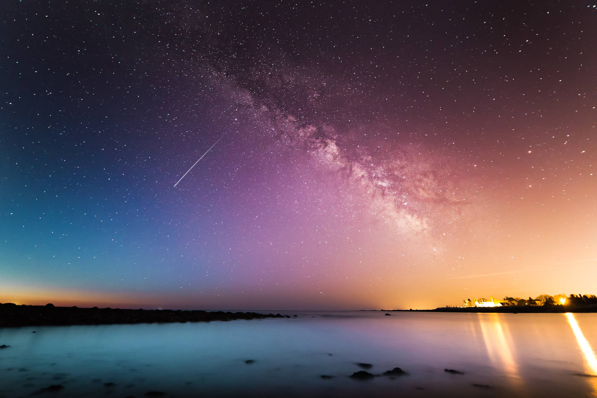夜晚平靜湖面上的銀河與流星，伴隨著溫暖的地平線光芒。