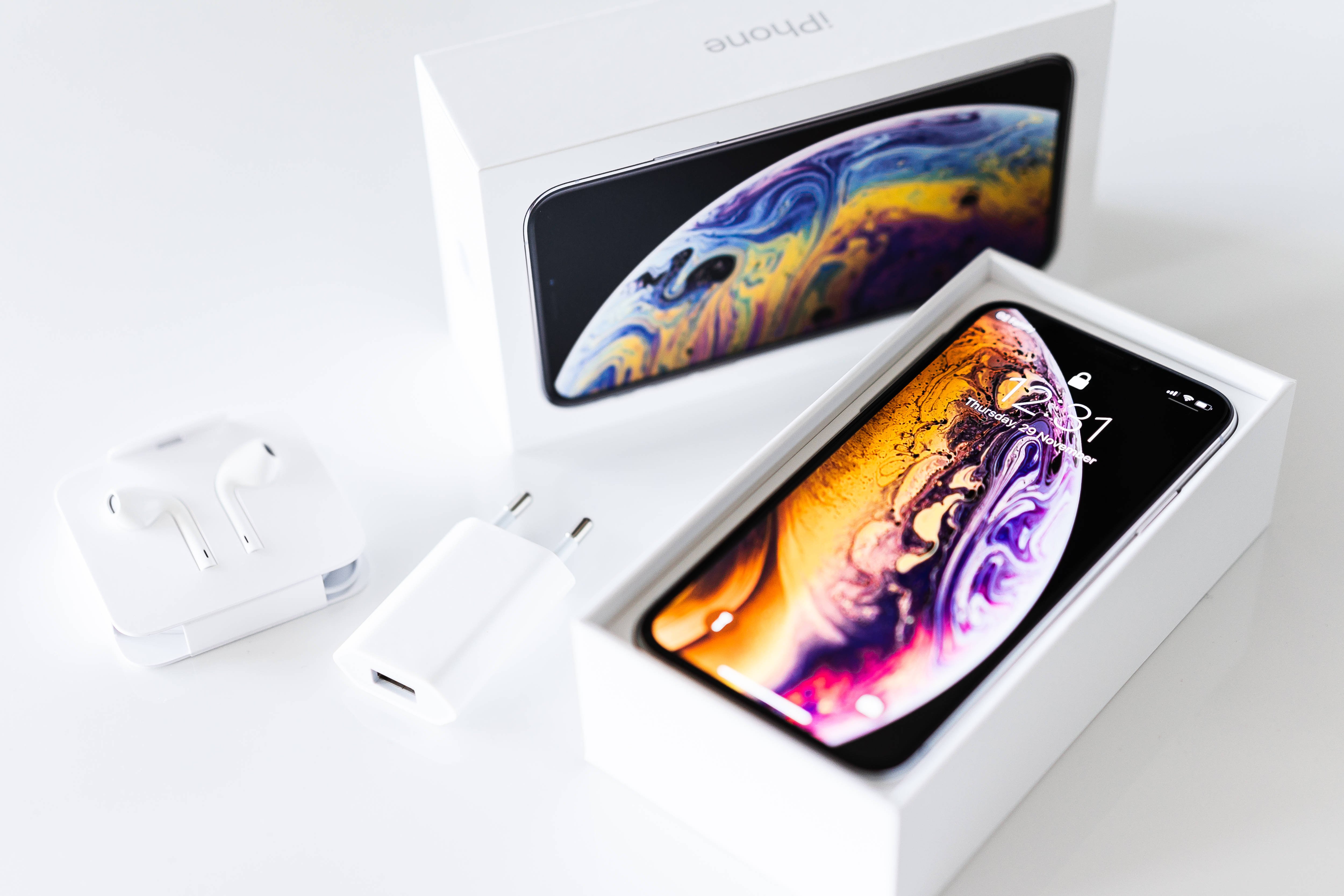 彩色月相手機鎖屏 壁紙 — 一部全新的iPhone XS打開放在盒中，耳機和充電器放在旁邊的潔白表面上。