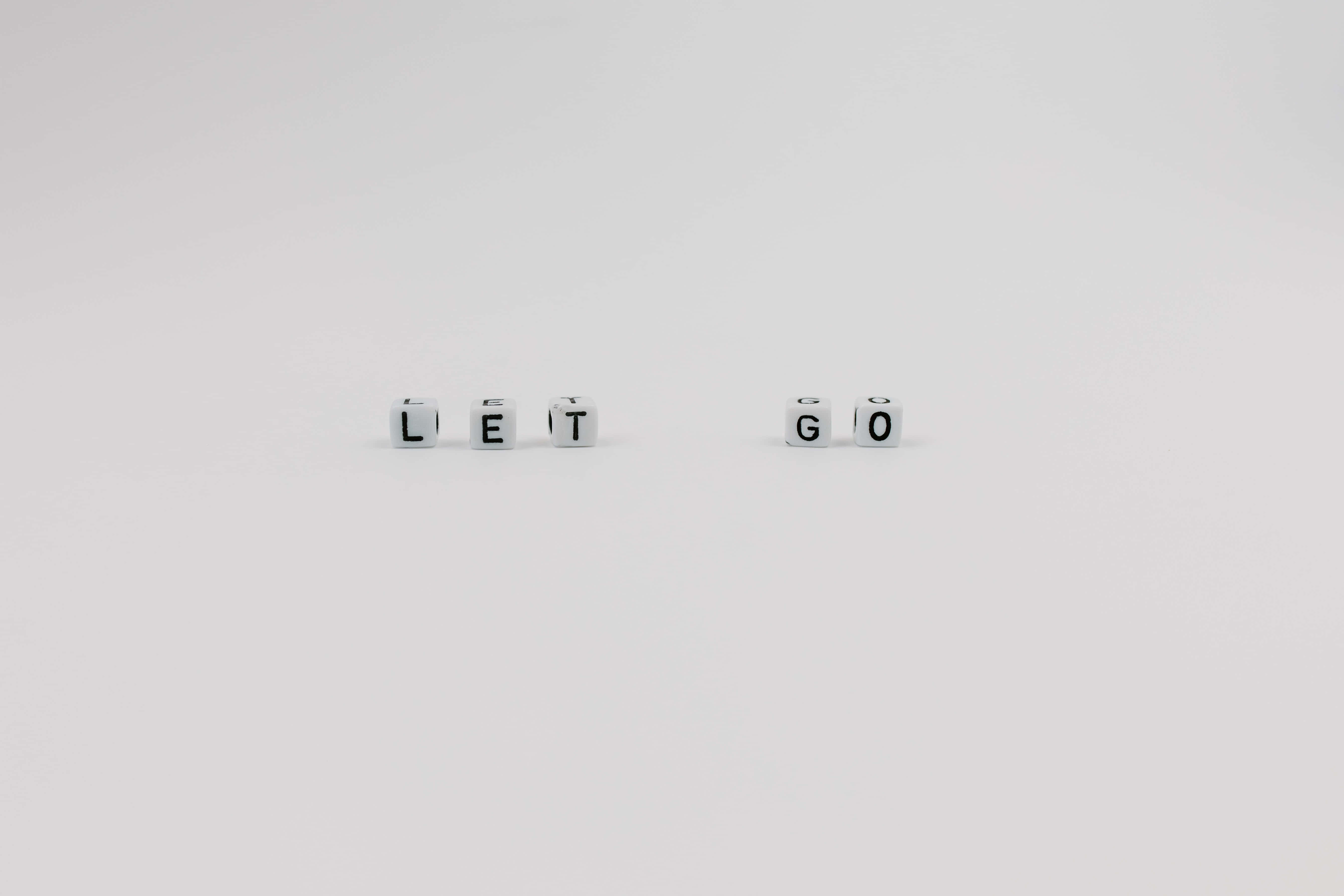 彩色積木拼出「放手」訊息 壁紙 — 白色字母方塊拼出 LET GO，間隔放置在純白表面上。