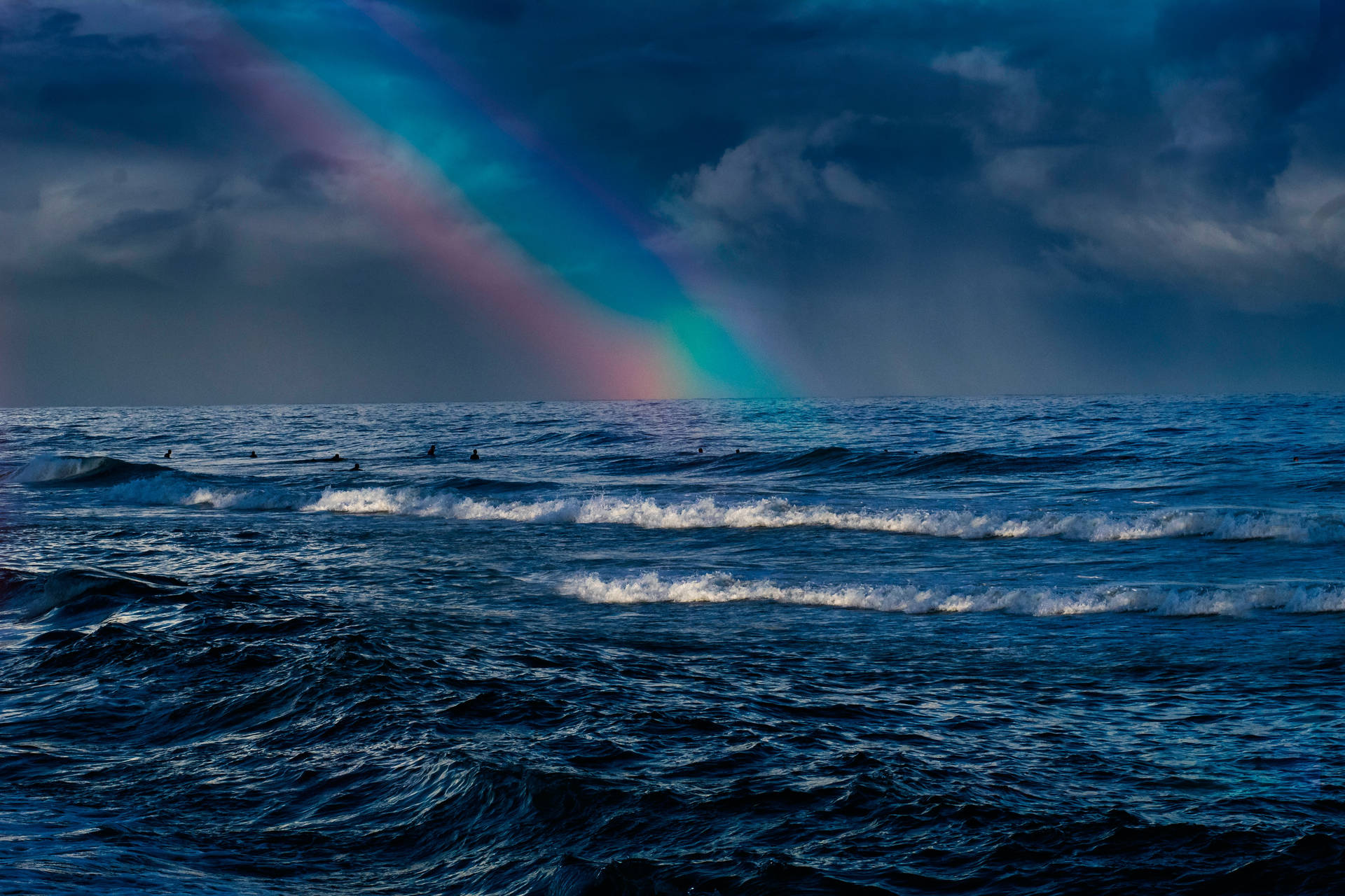 衝浪者在暴風雨的天空下，於海洋波浪中乘風破浪，天空掛著彩虹。