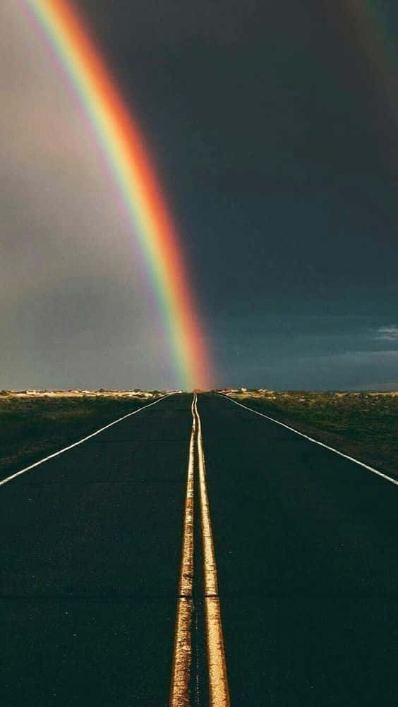 一道彩虹拱起在一條長長的空曠道路上，下方是暴風雨的天空。