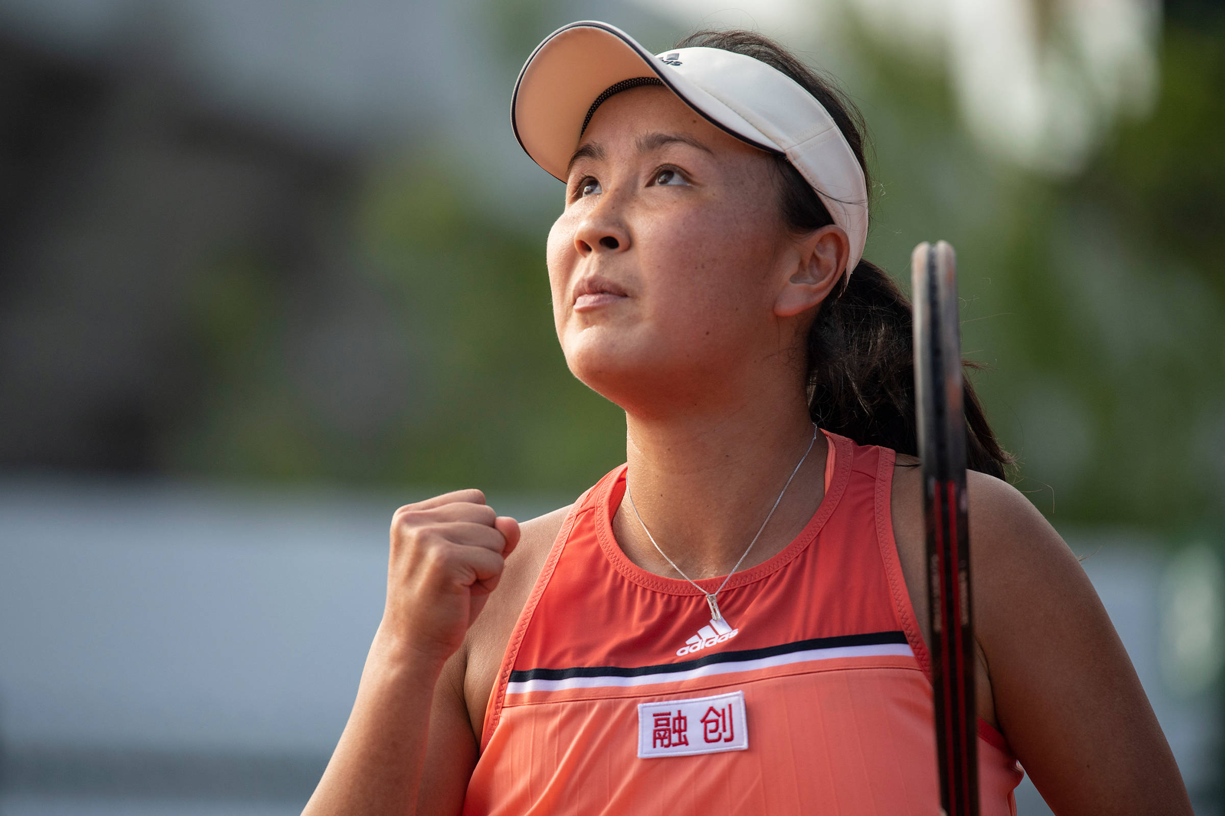 彭帥慶祝勝利 壁紙 — 一位專注的女網球選手穿著橙色裝備，在戶外握緊拳頭並拿著球拍。